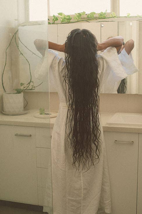 Person with long hair standing in front of a bathroom mirror.
