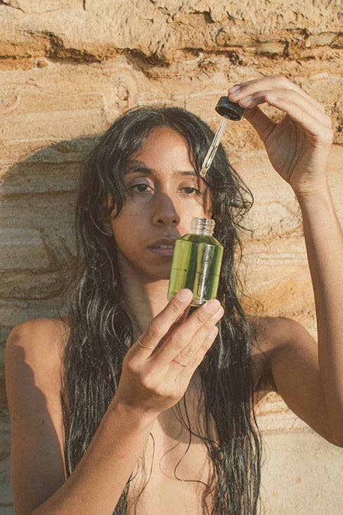 Woman holding a bottle of green liquid against a stone wall
