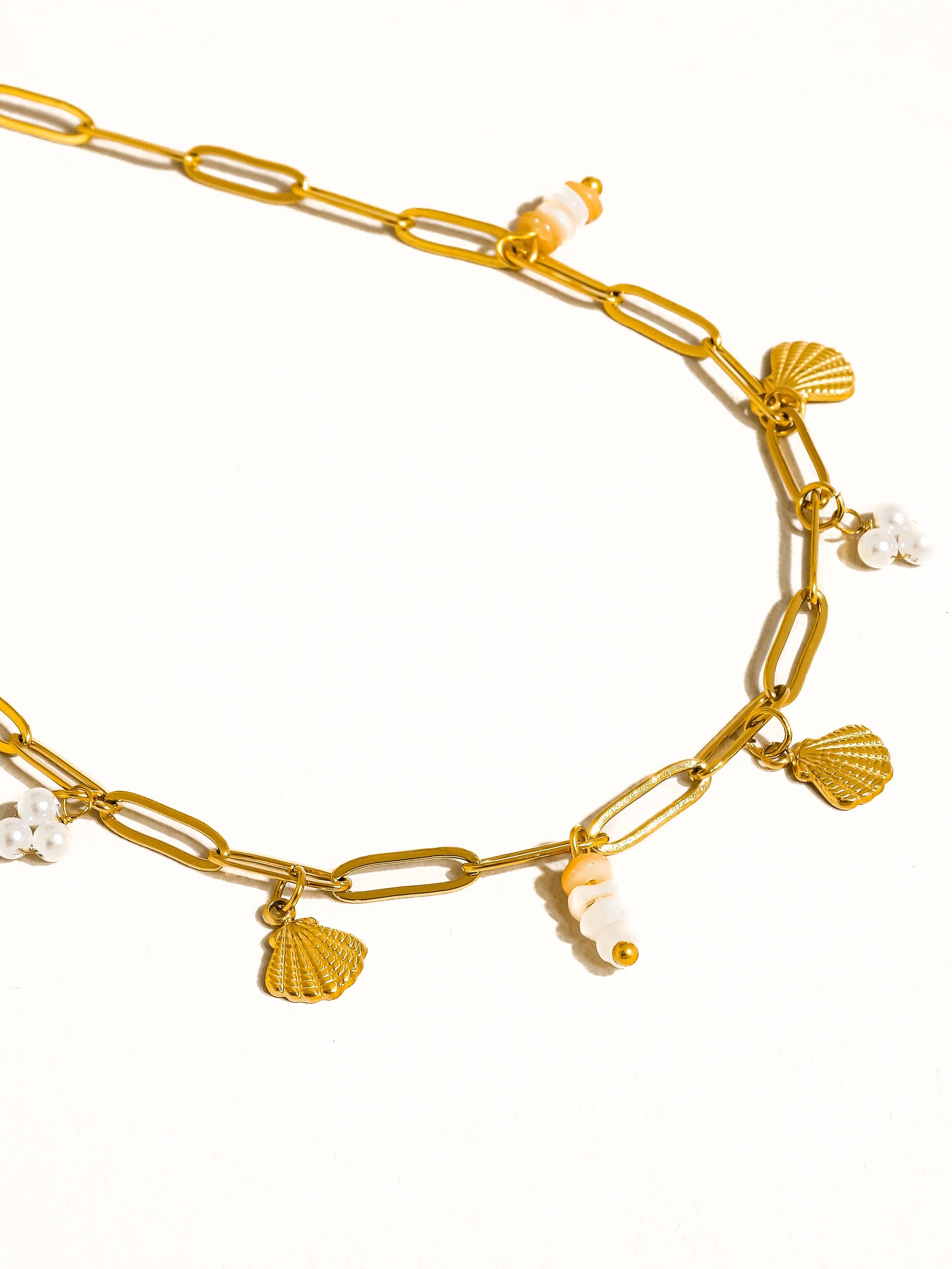 Gold chain necklace with shell and pearl charms on a white background