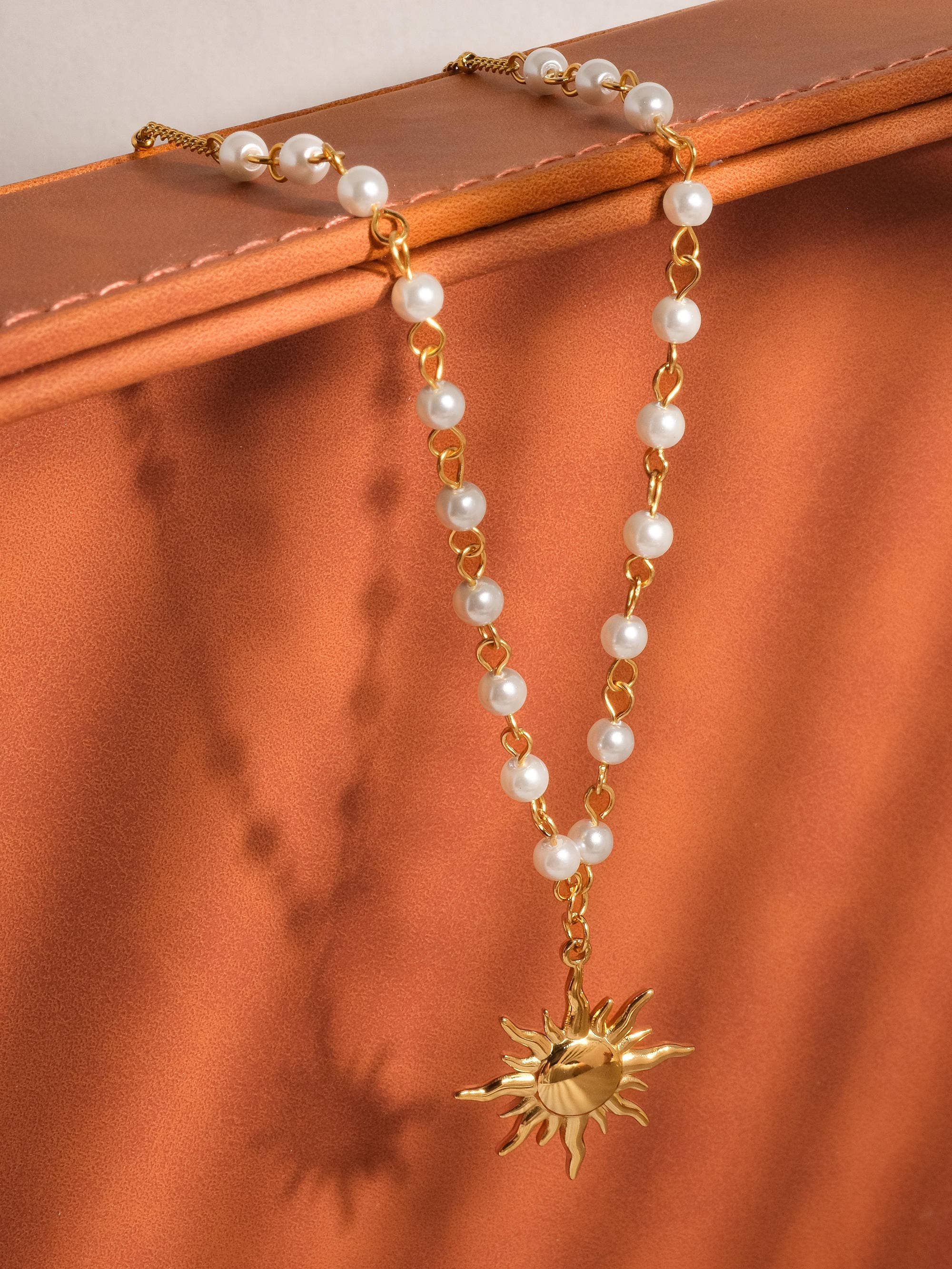 Pearl necklace with a gold sun pendant on a brown surface