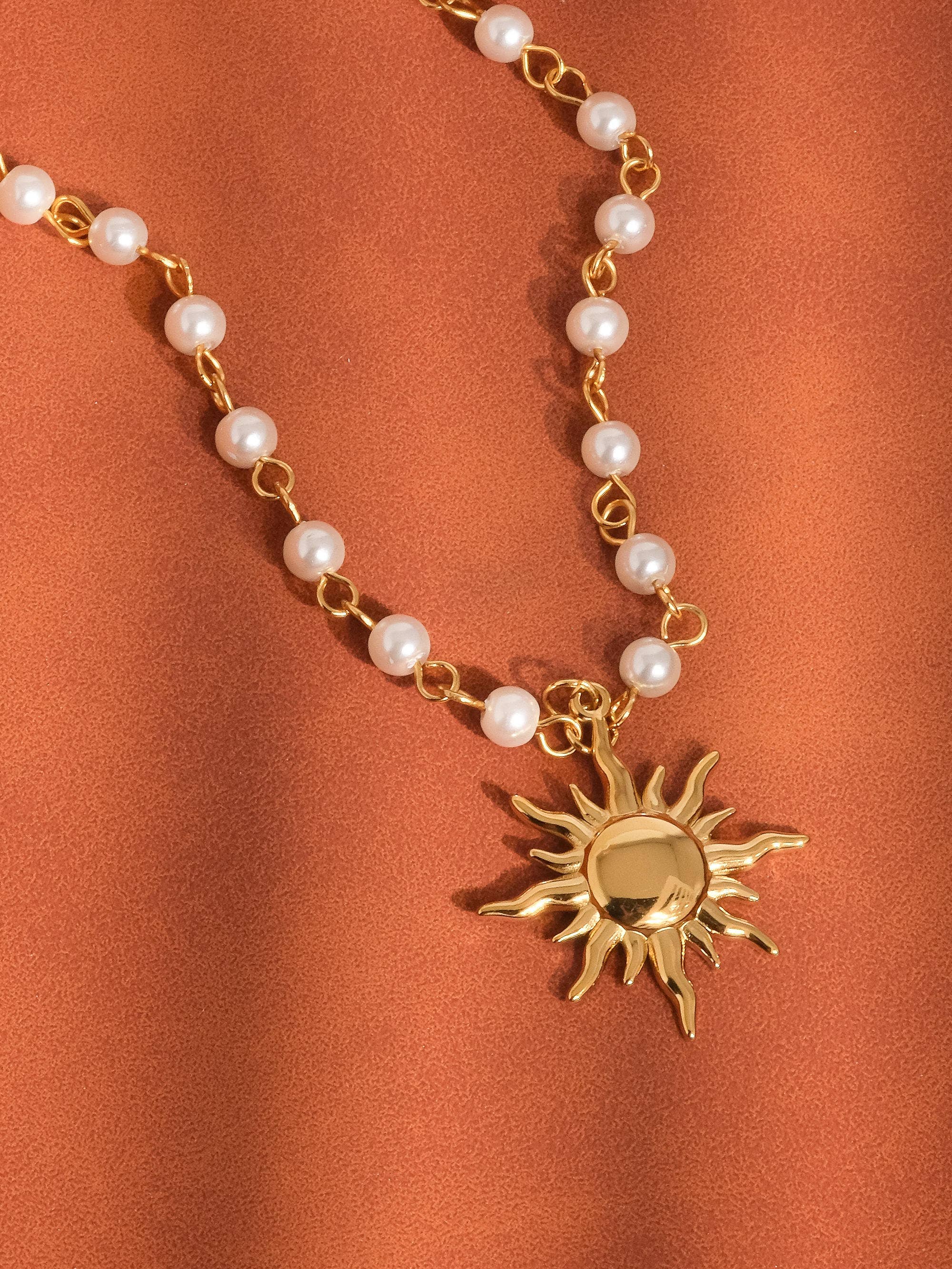 Necklace with pearl beads and a gold sun pendant on an orange background