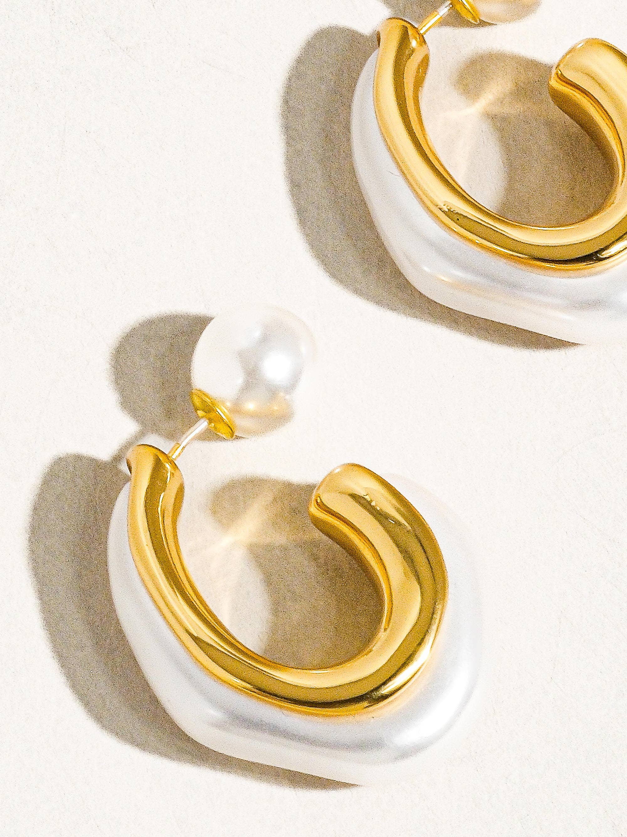 Gold and white earrings on a light background