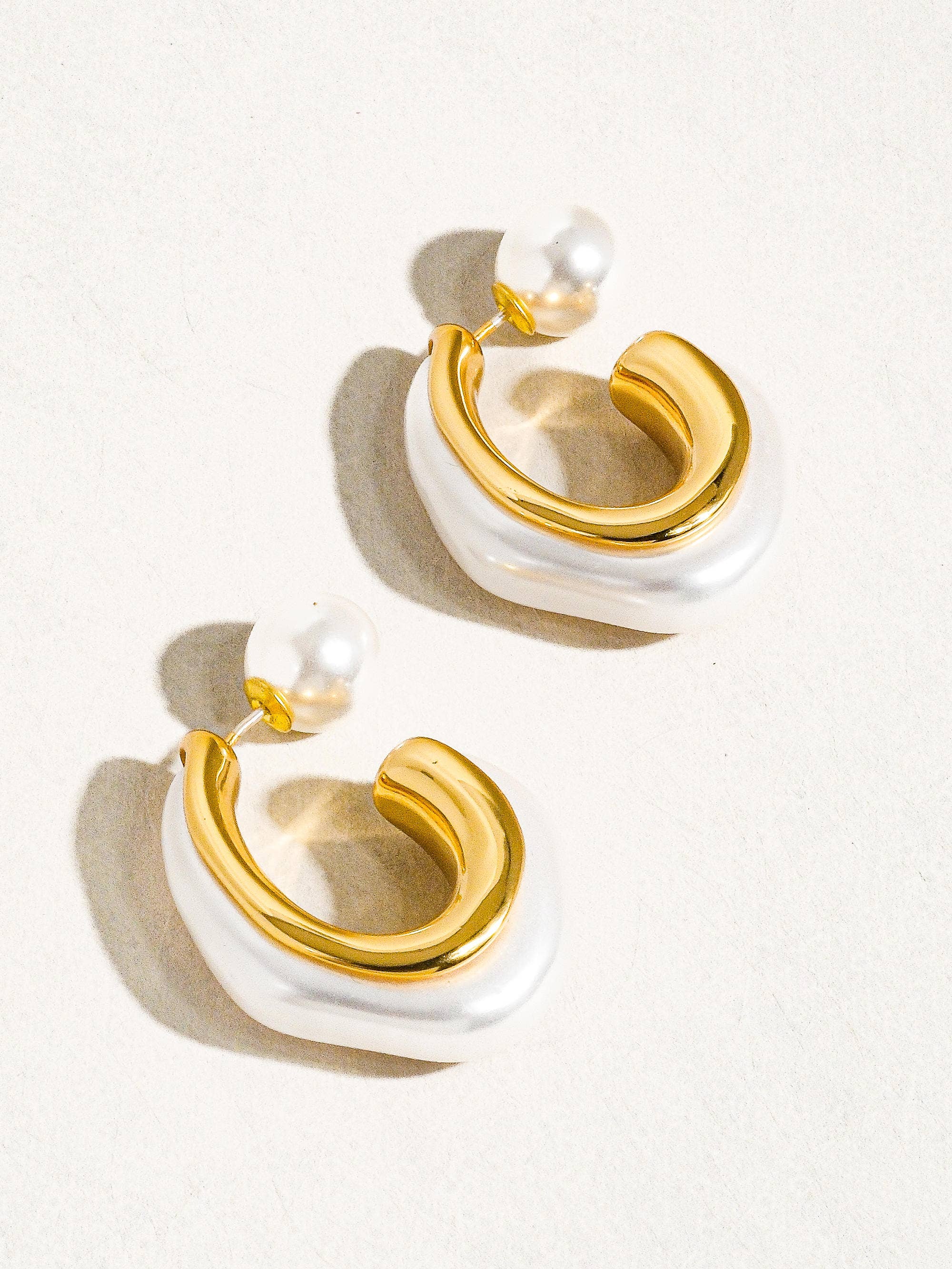 Gold and white earrings with pearls on a light background