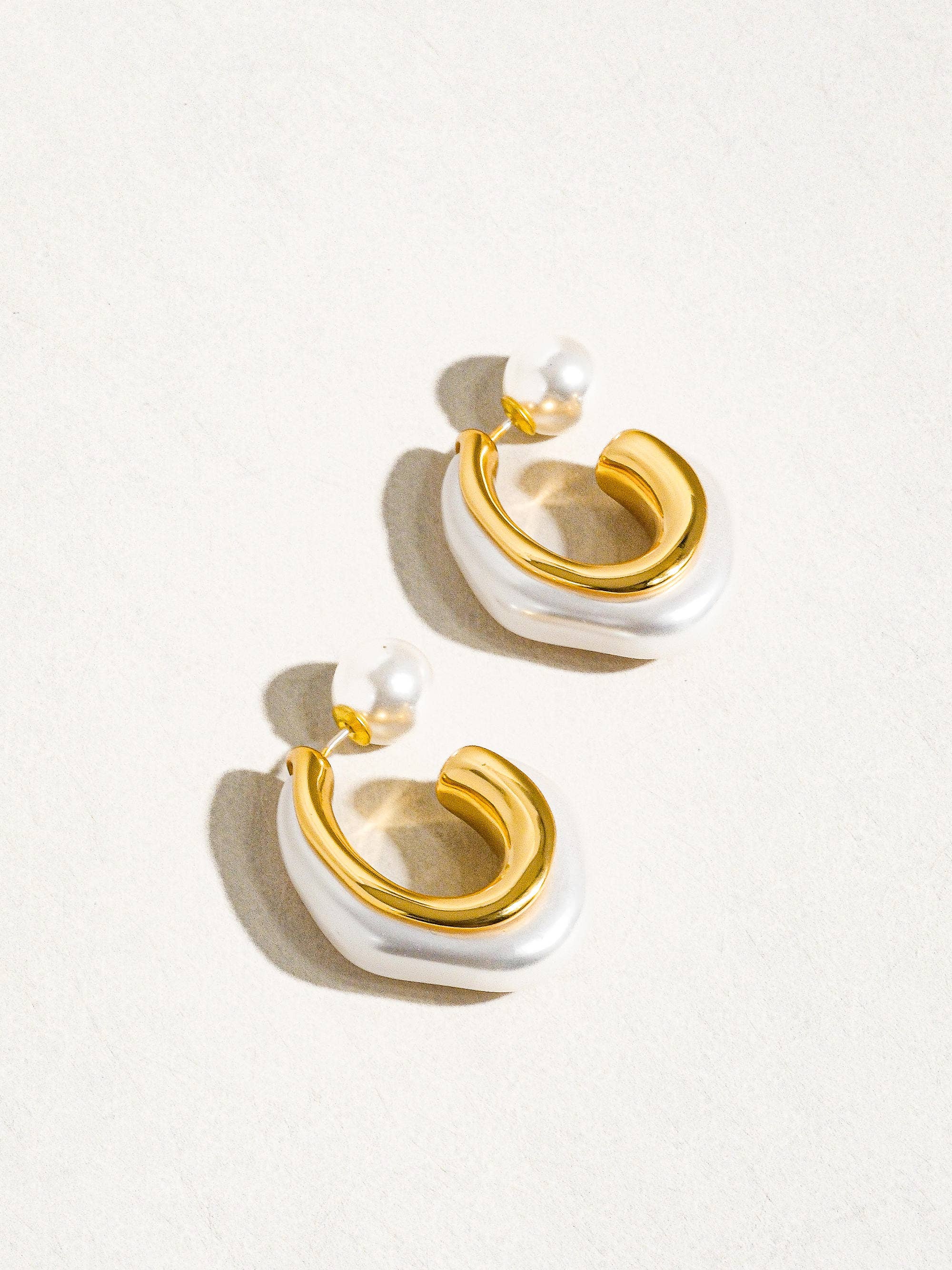 Gold and white earrings on a light background