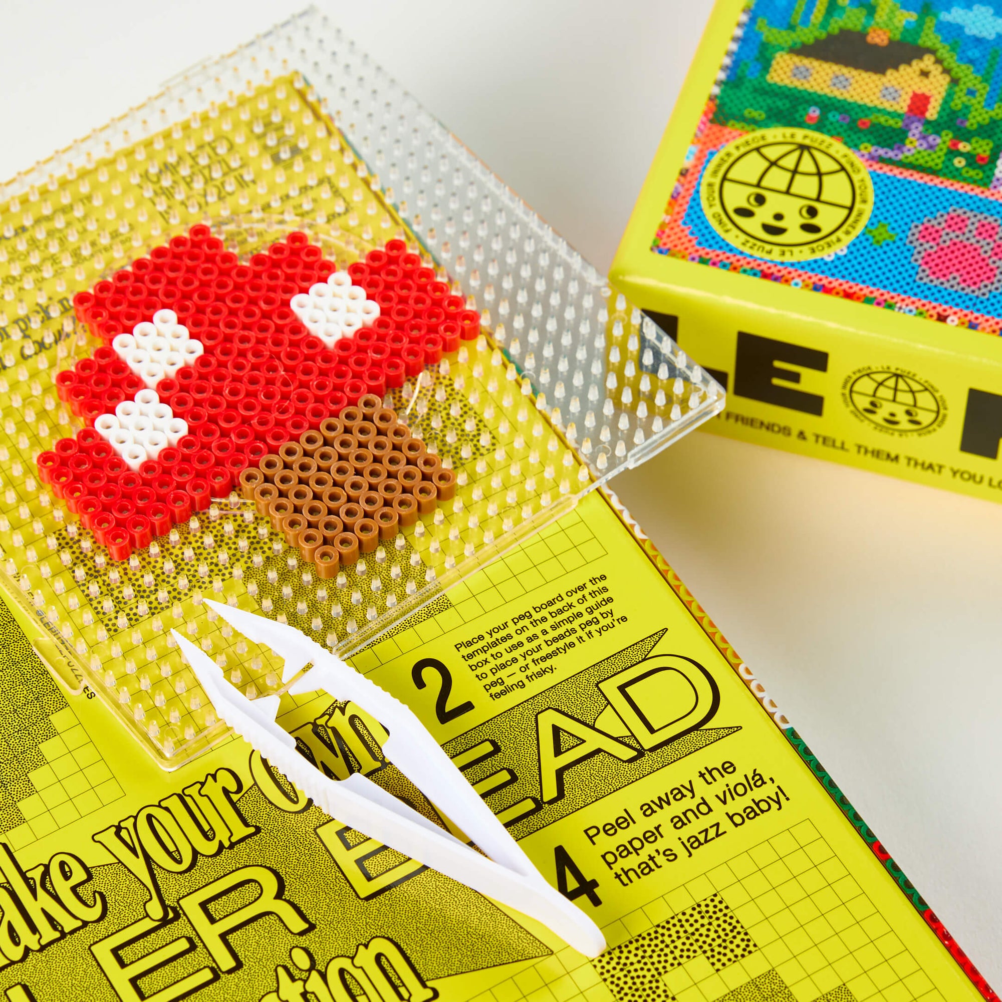 Perler bead creation with red, white, and brown beads on a yellow box with text.