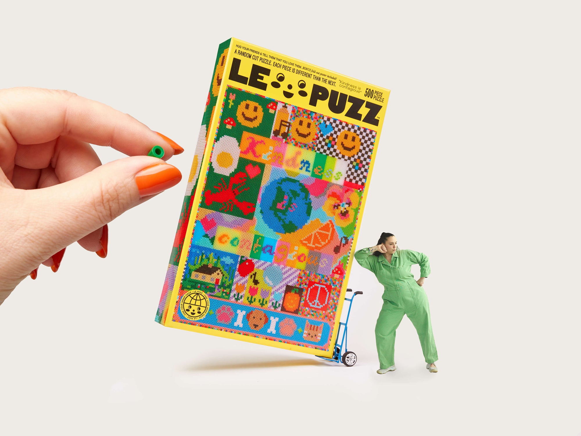 Colorful puzzle box with 'LE PUZZ' branding held by a hand, with a small figure in a green outfit standing next to it.