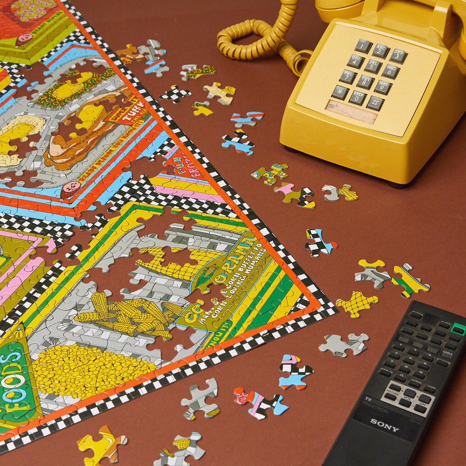 Puzzle with colorful pieces on a table next to a yellow phone and remote control.