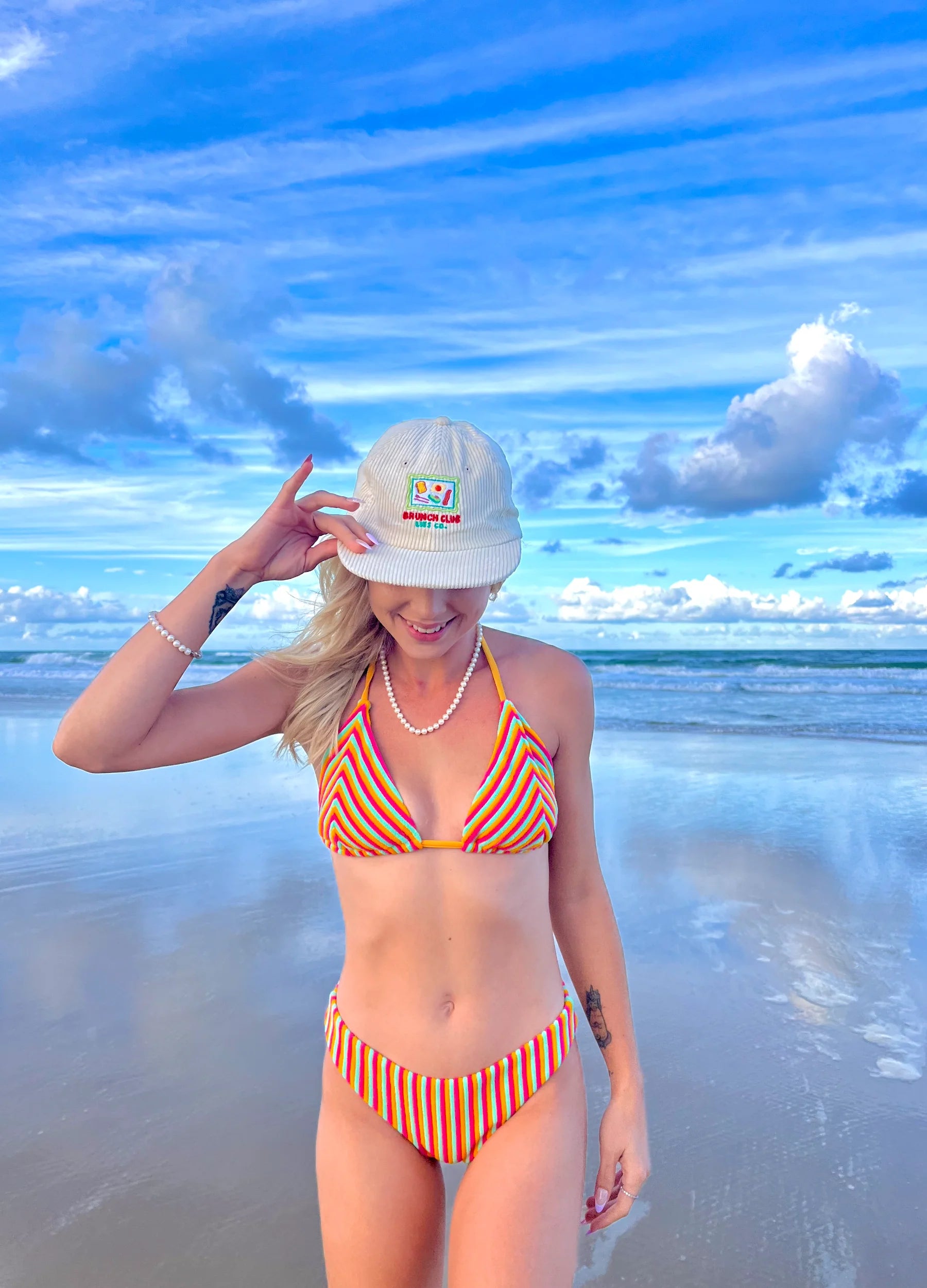 Woman in a striped bikini and cap on a beach with blue sky and ocean.