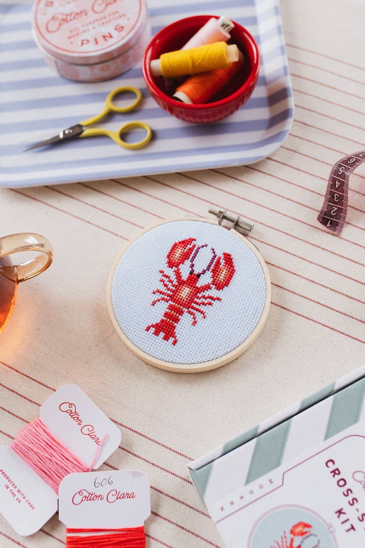 Cross-stitch kit with lobster design on a table with embroidery supplies.