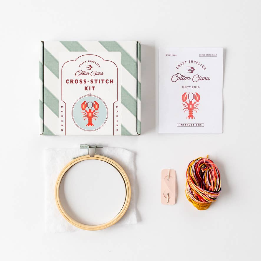 Cross-stitch kit with hoop, yarn, and packaging on a white background