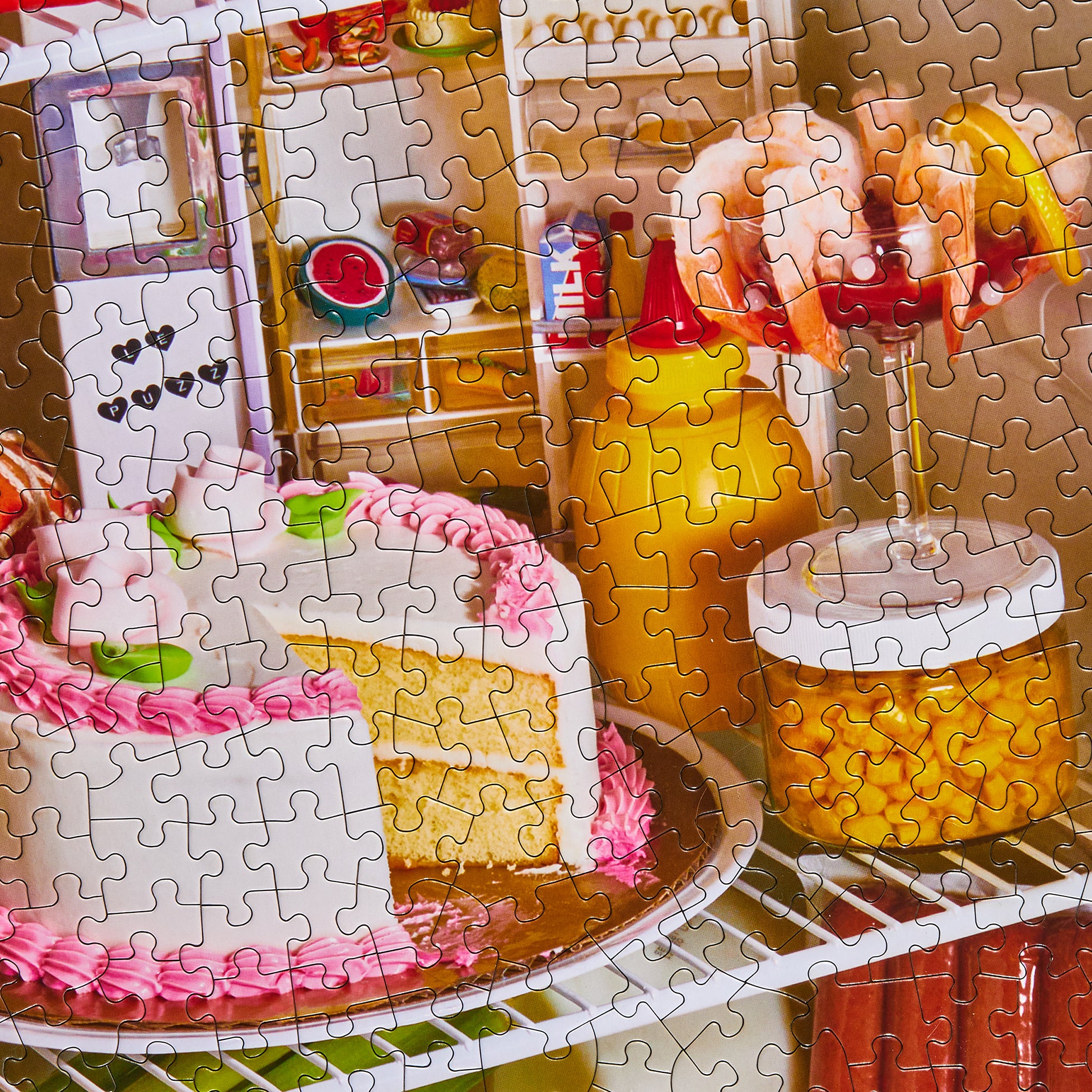 Close-up of completed Le Puzz Midnight Snack puzzle featuring a cake, sauce bottle, and prawn cocktail