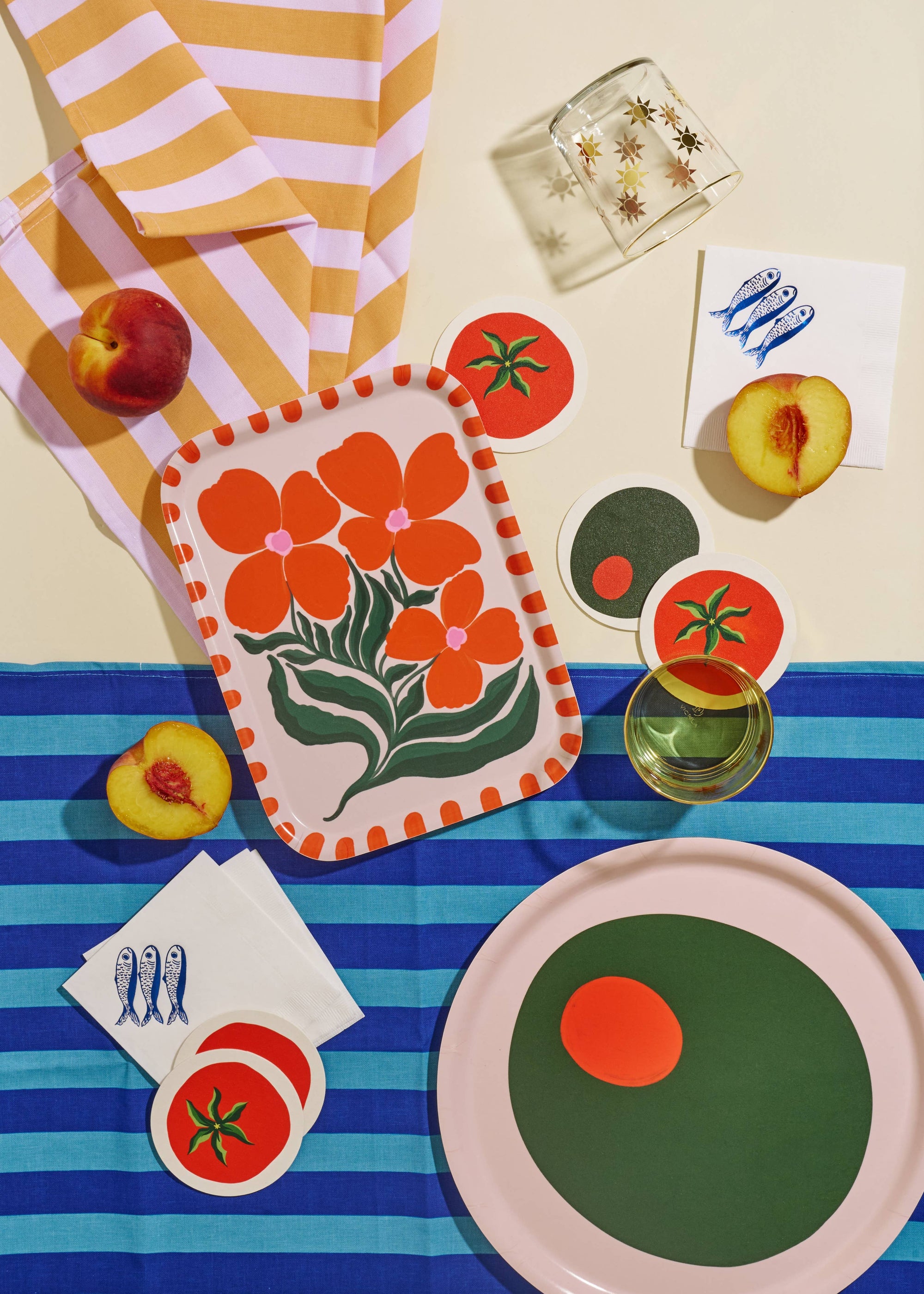 Colorful table setting with floral towel, plates, and coasters on a striped tablecloth.