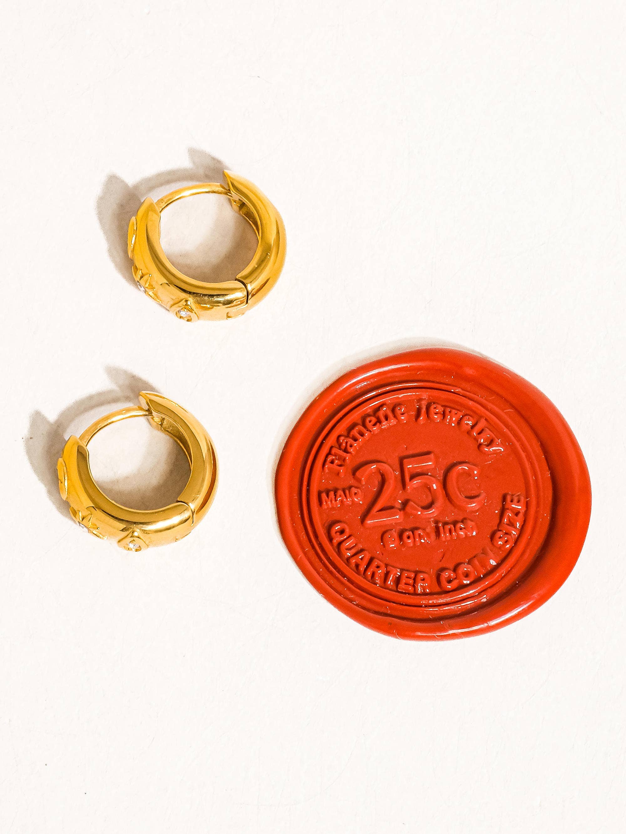 Two gold hoop earrings and a red stamp with '25C' on a white background