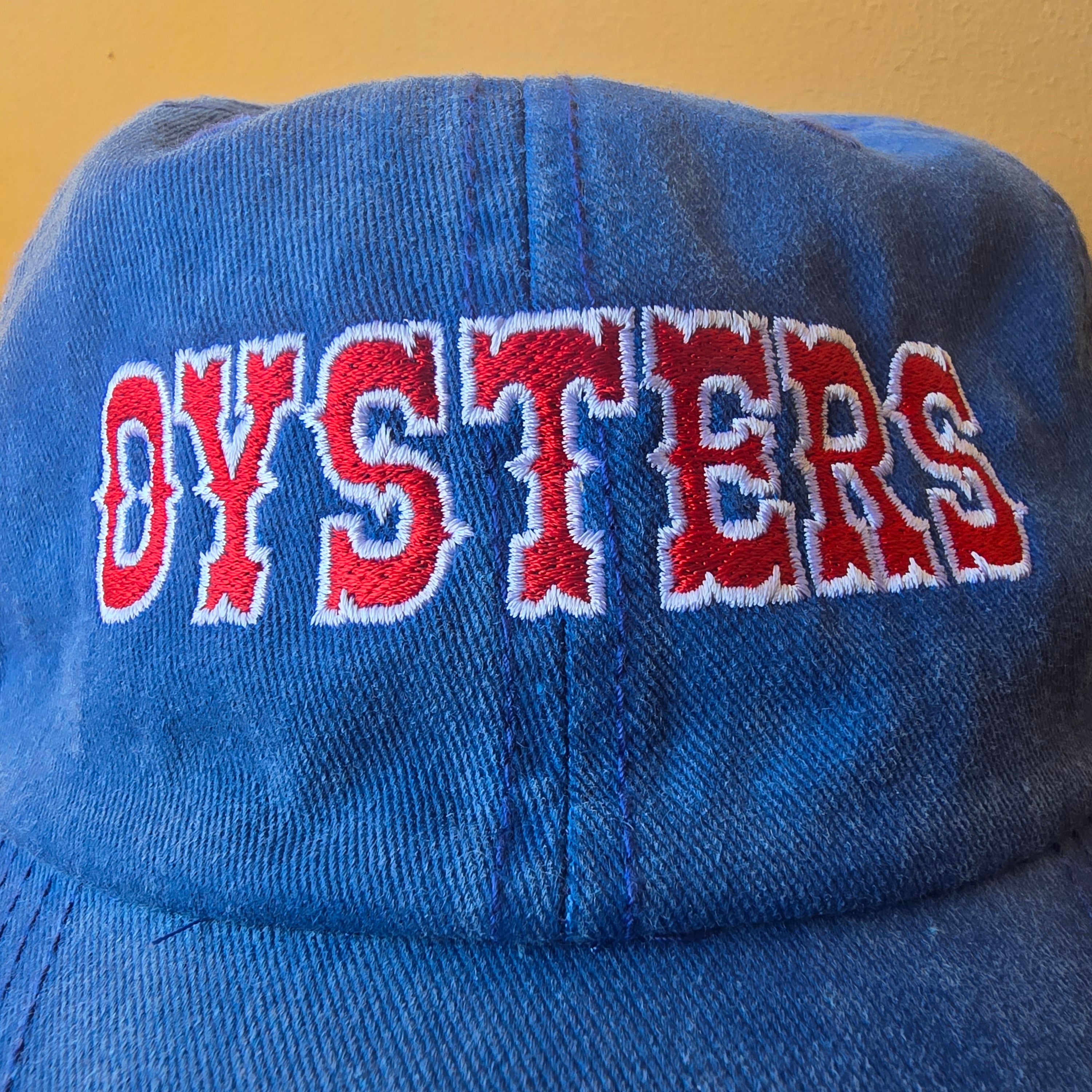 Blue cap with 'OYSTERS' embroidered in red and white on a wooden surface.