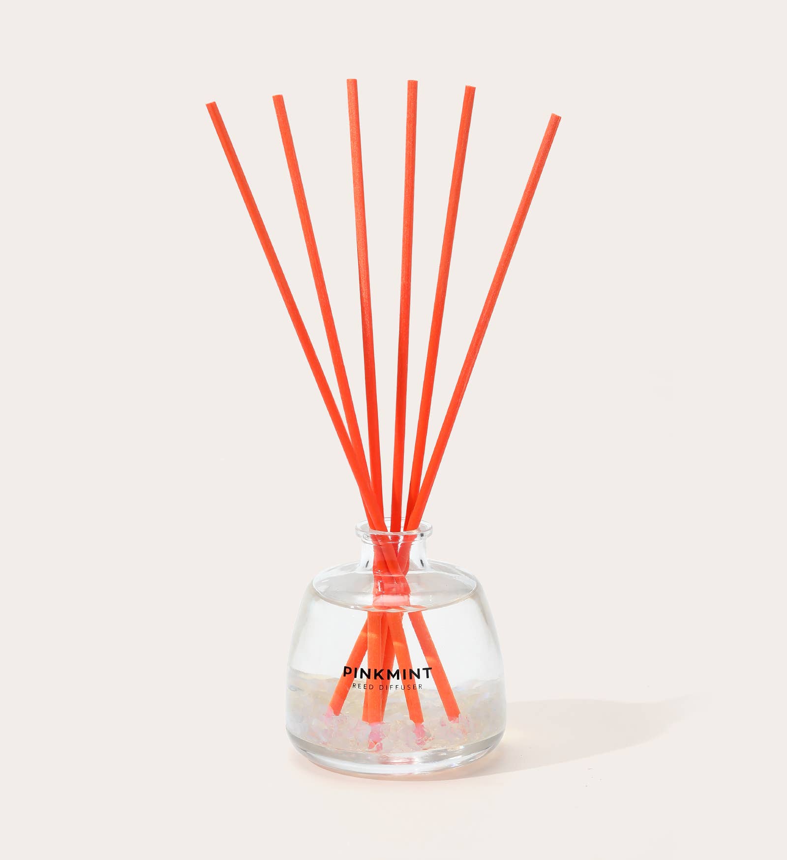 Reed diffuser with orange sticks in a clear bottle on a light background