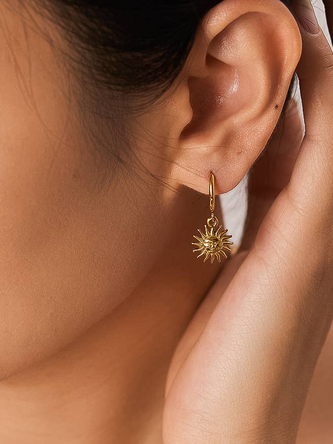Gold hoop earring with sun design worn by a person