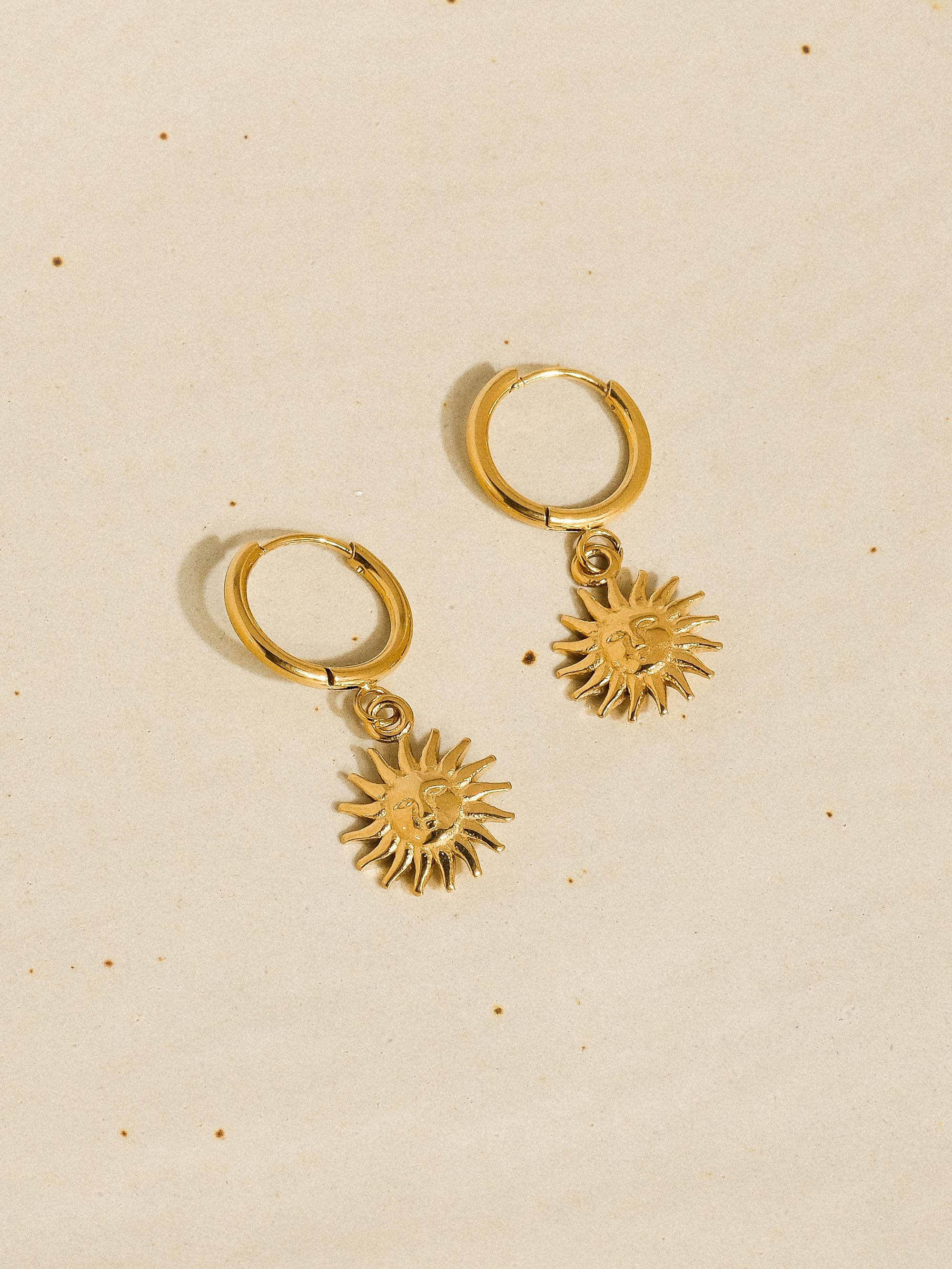 Gold hoop earrings with sun-shaped charms on a beige background