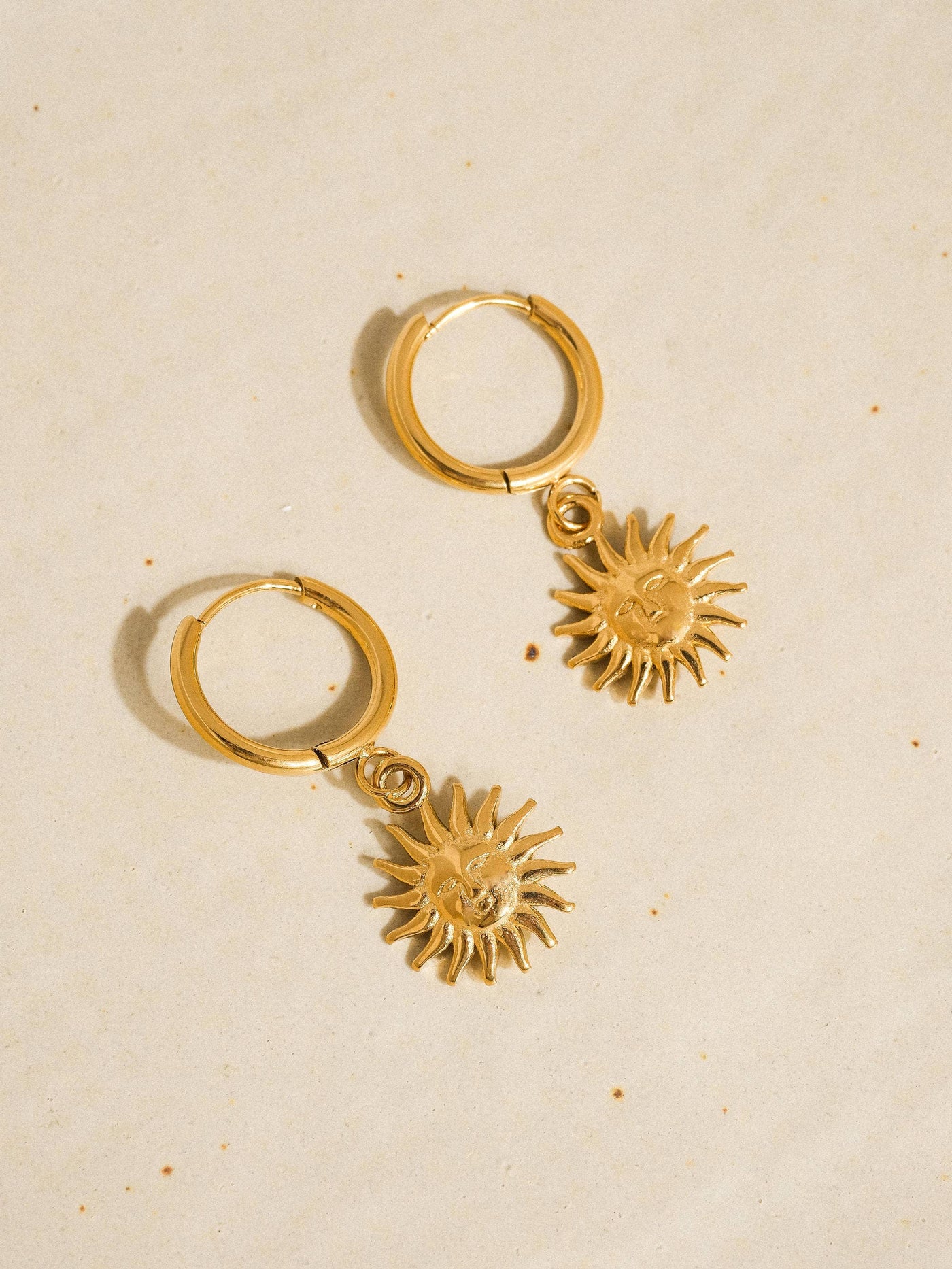 Gold hoop earrings with sun-shaped charms on a beige background