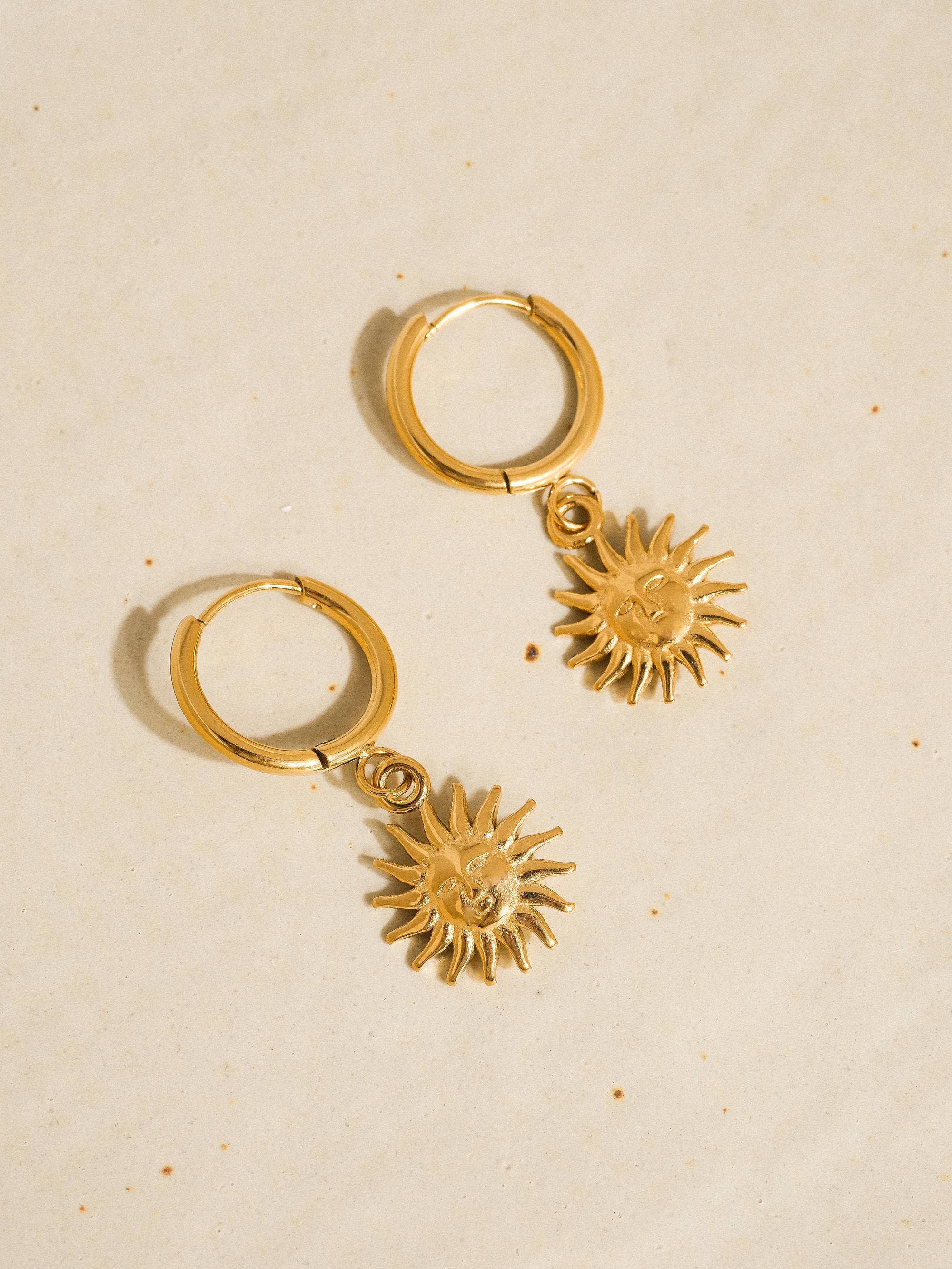 Gold hoop earrings with sun-shaped charms on a beige background