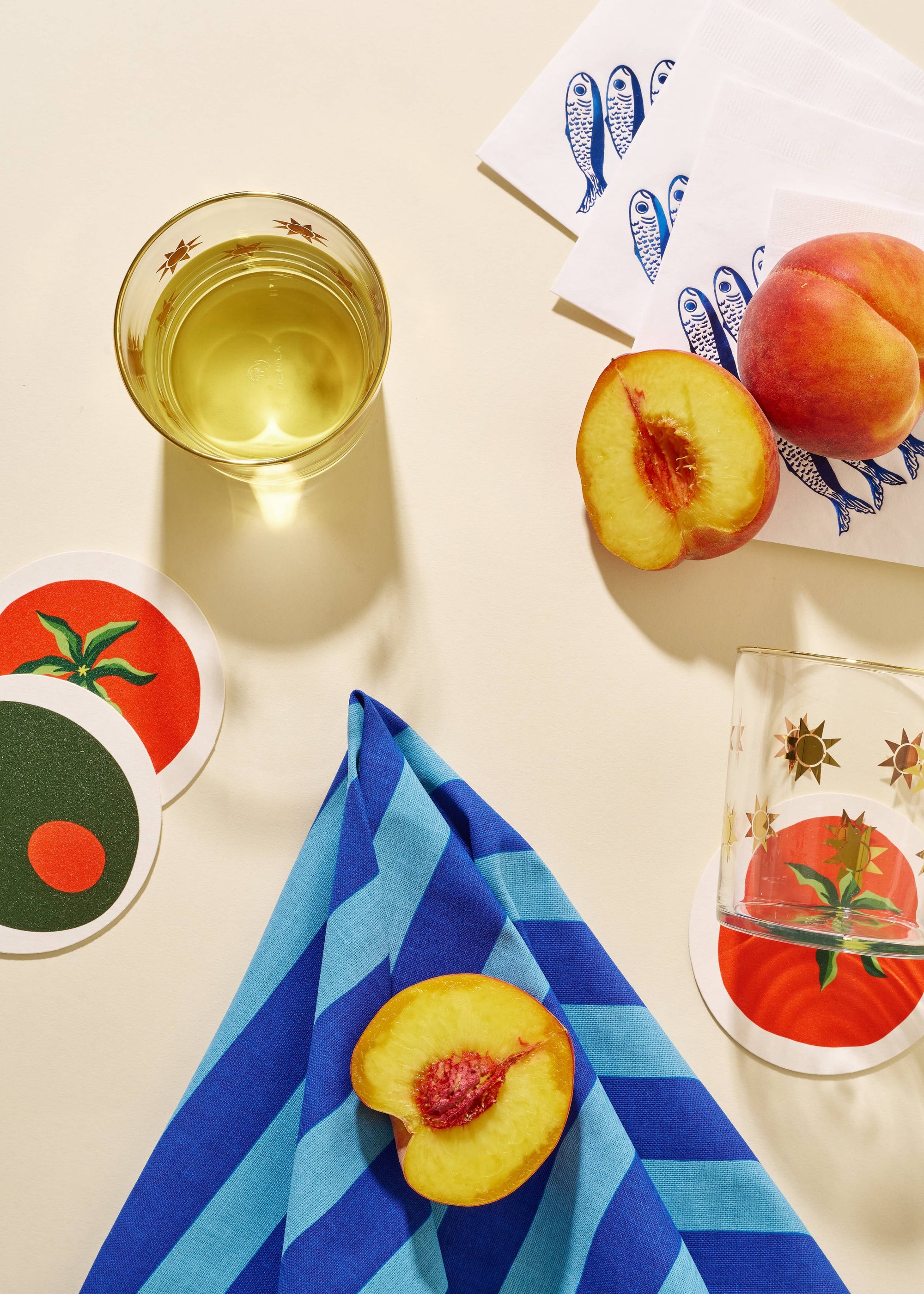 Peaches, a glass of white wine, and coasters with tomato design on a light surface.