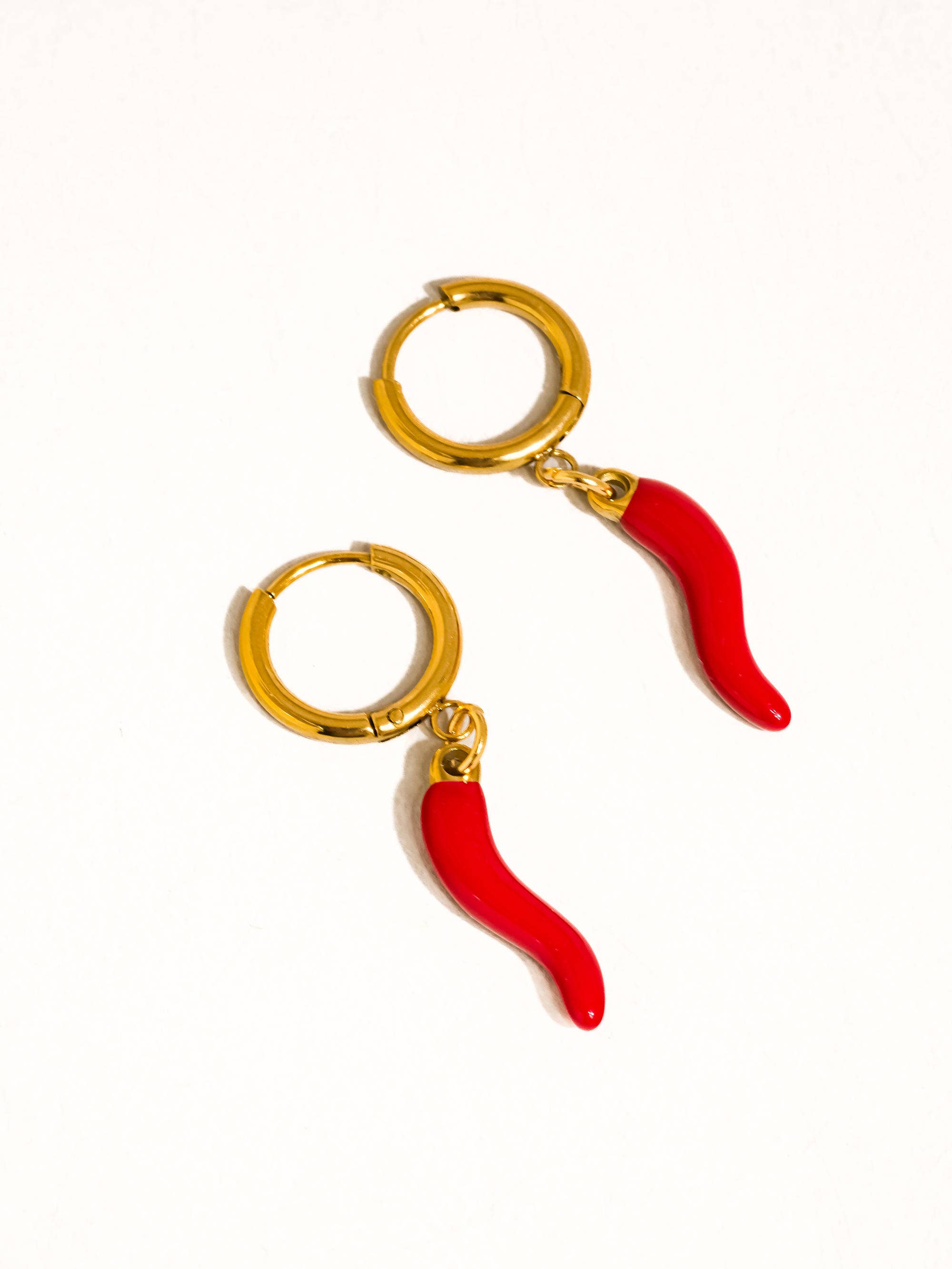 Gold hoop earrings with red chili pepper charms on a white background