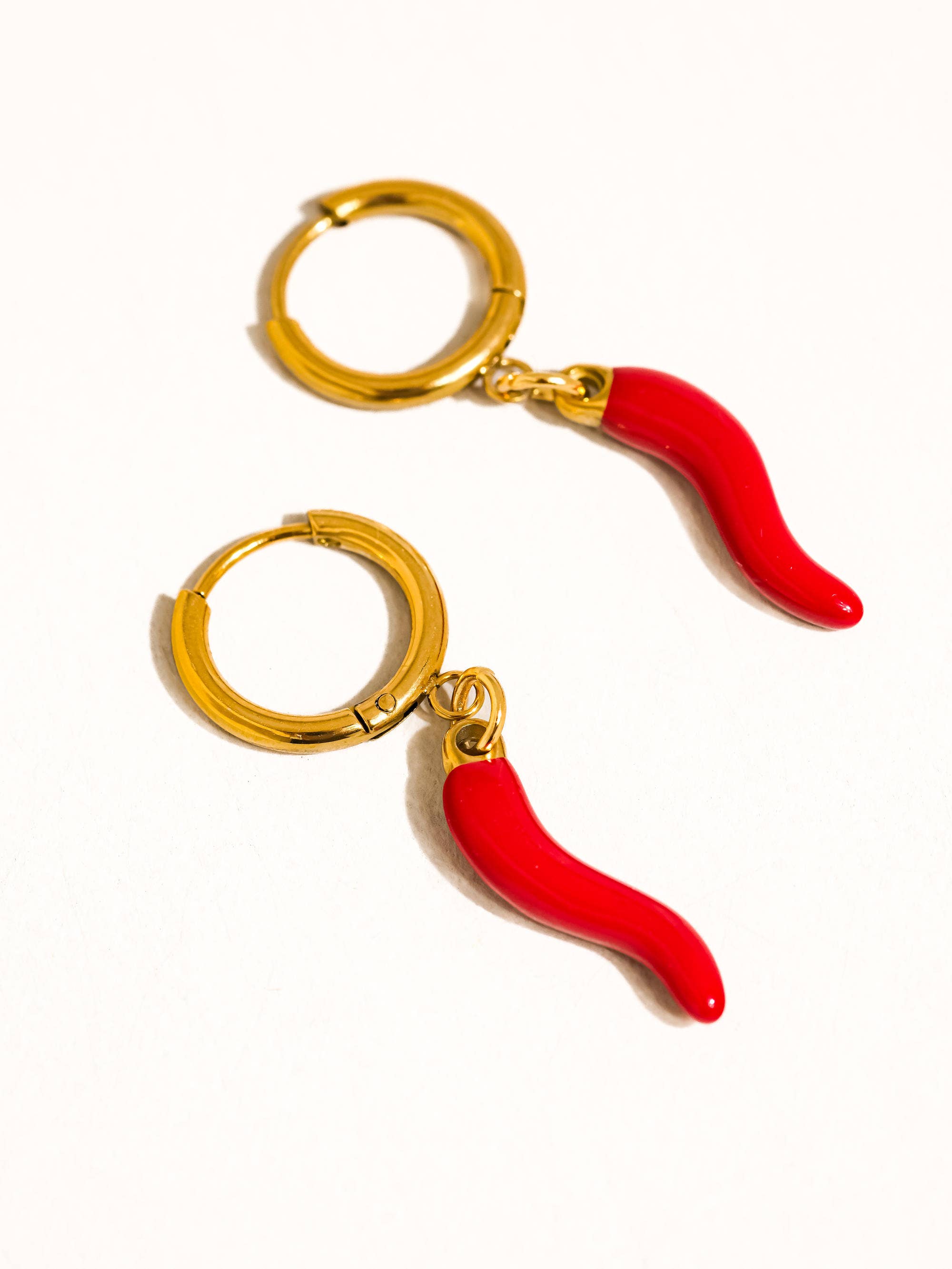 Pair of gold hoop earrings with red chili pepper charms on a white background