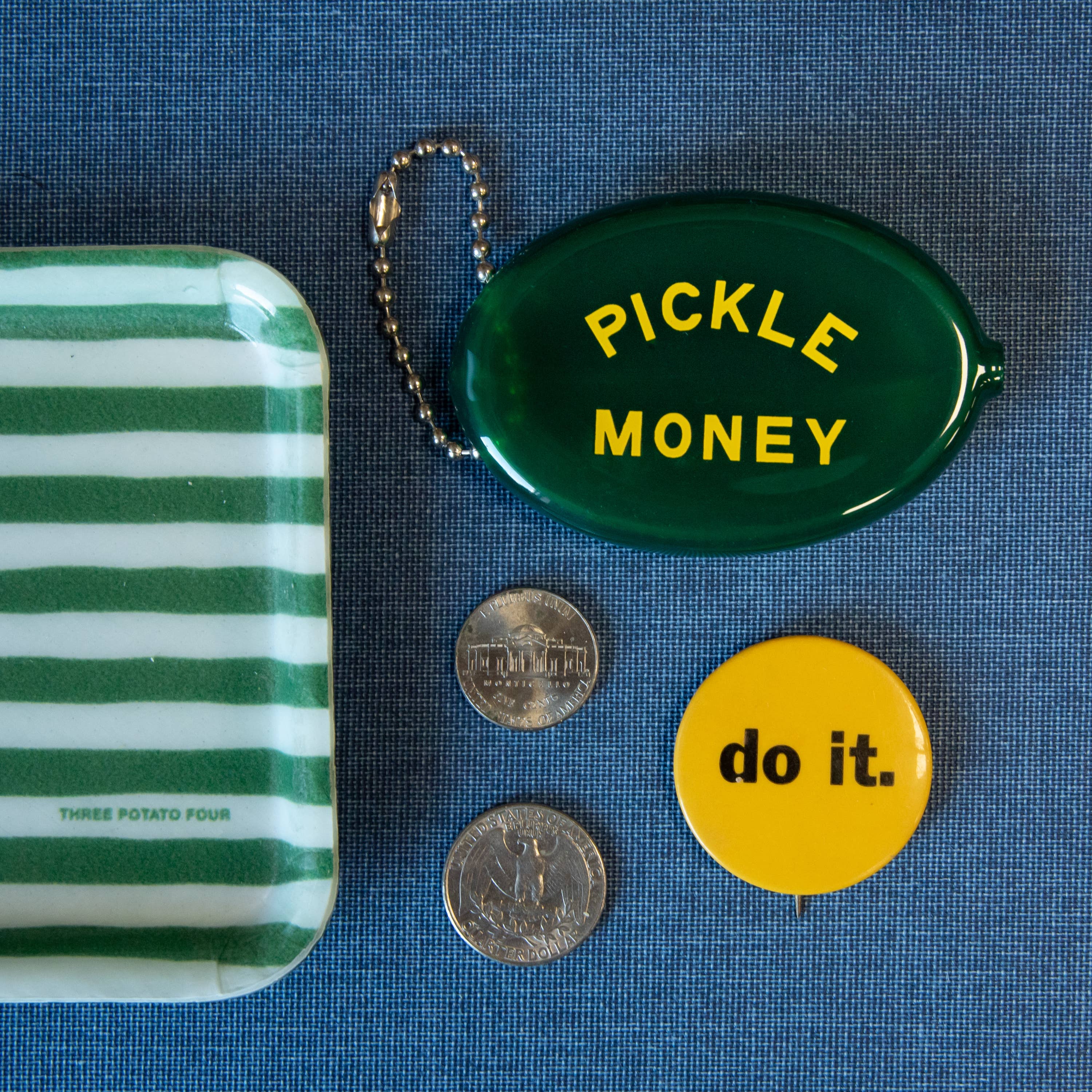 Green and white striped tray, 'Pickle Money' keychain, coins, and 'do it.' button on a blue background