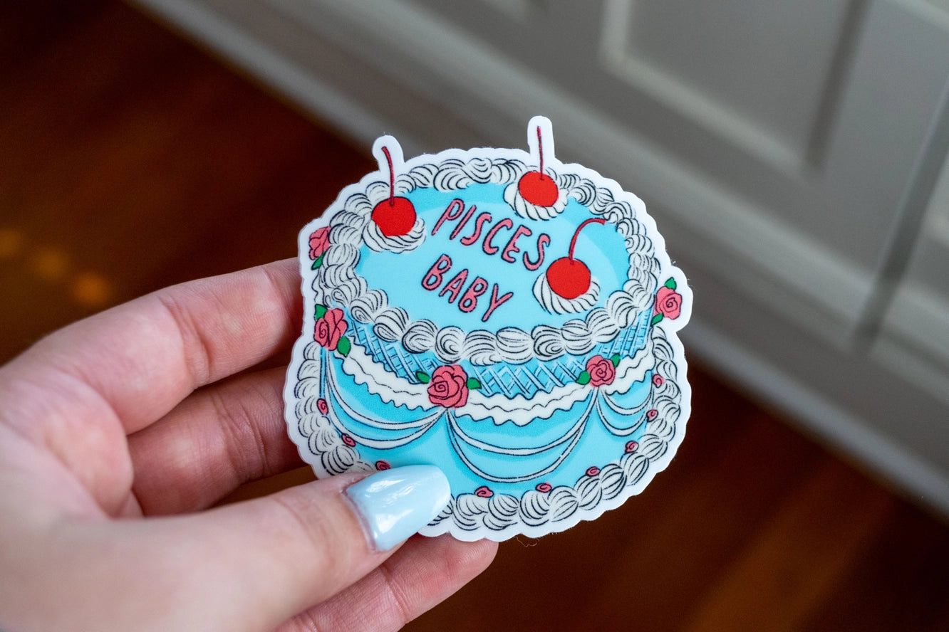 Sticker of a cake with 'Pisces Baby' text held by a hand.