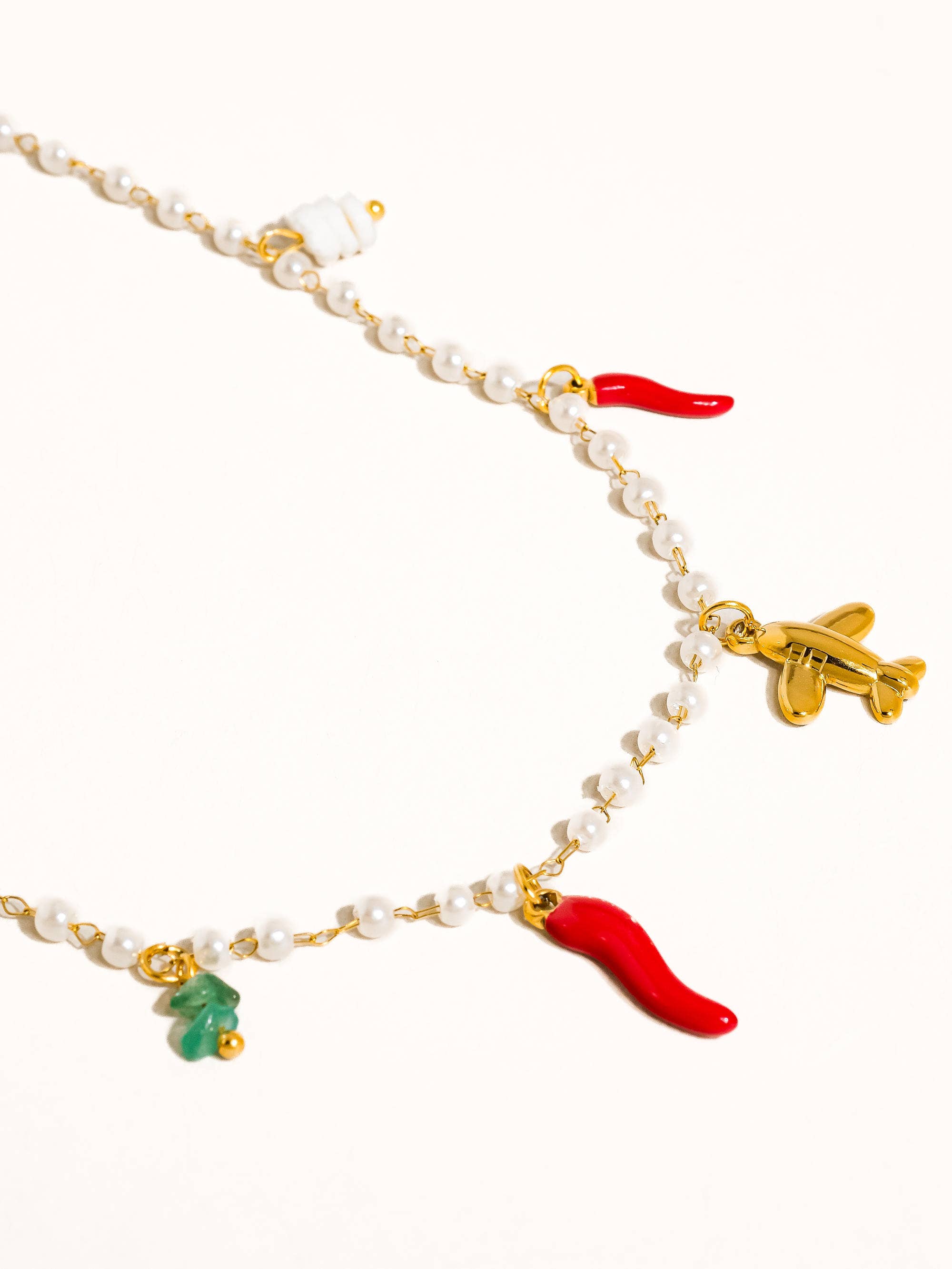 Necklace with various charms including a red chili pepper, airplane, and green leaf on a white background