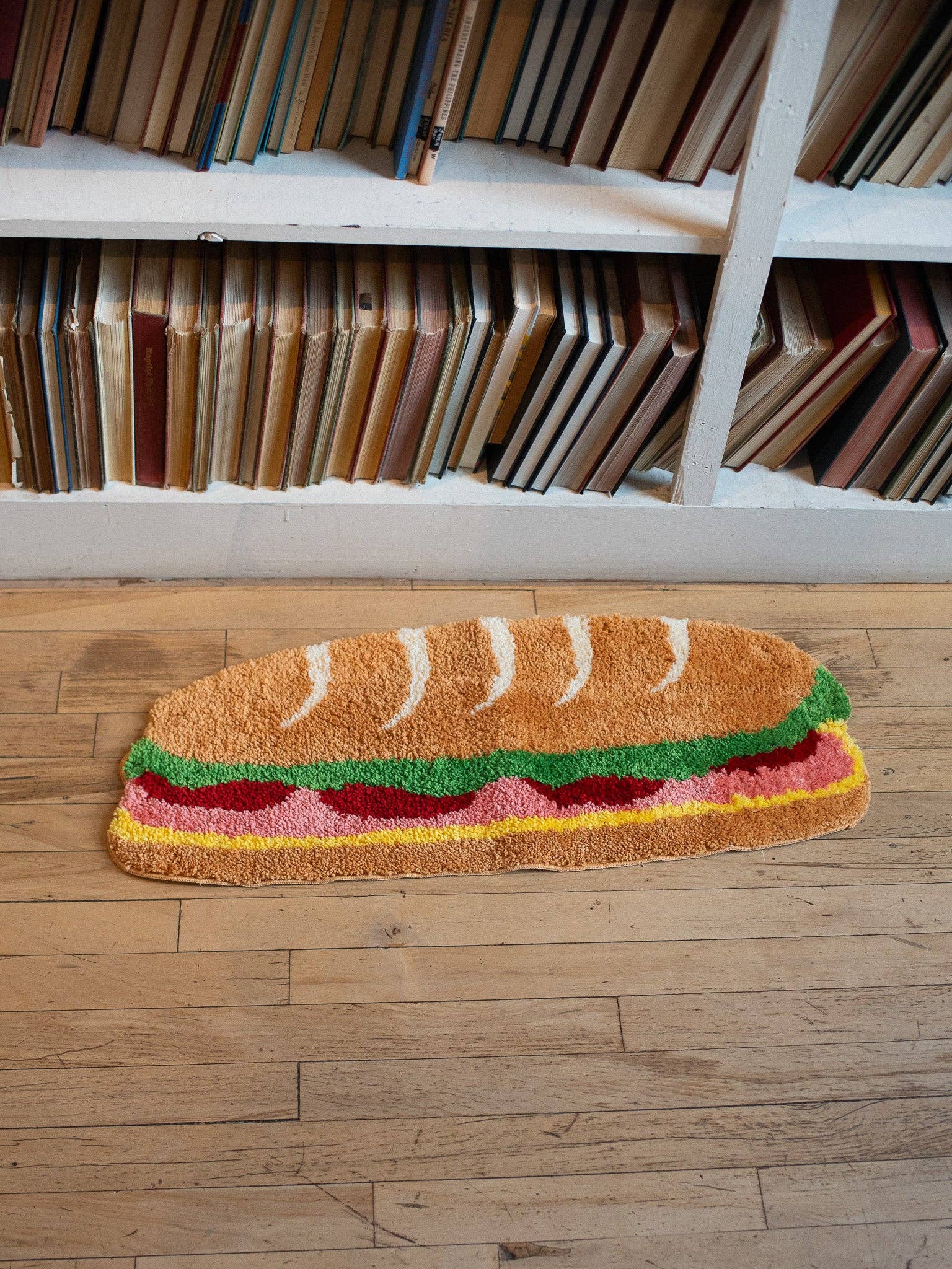 Sandwich-shaped doormat on a wooden floor with a bookshelf in the background