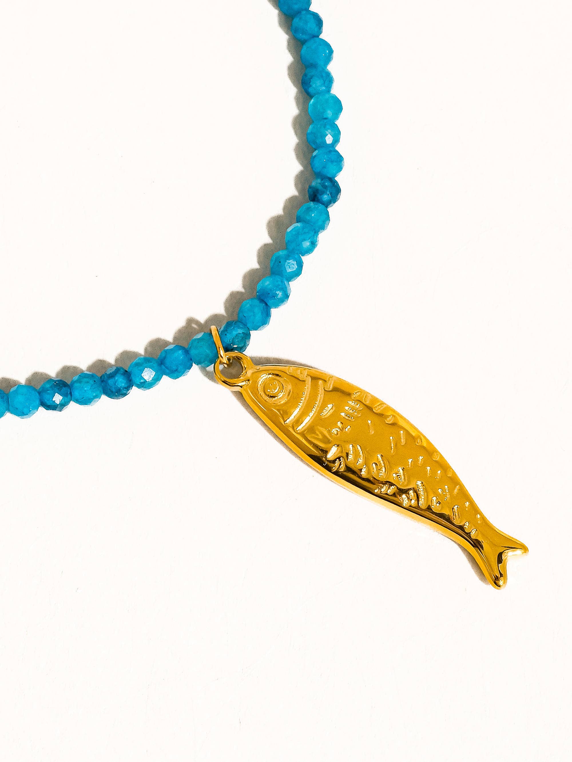 Necklace with blue beads and a gold fish pendant on a white background
