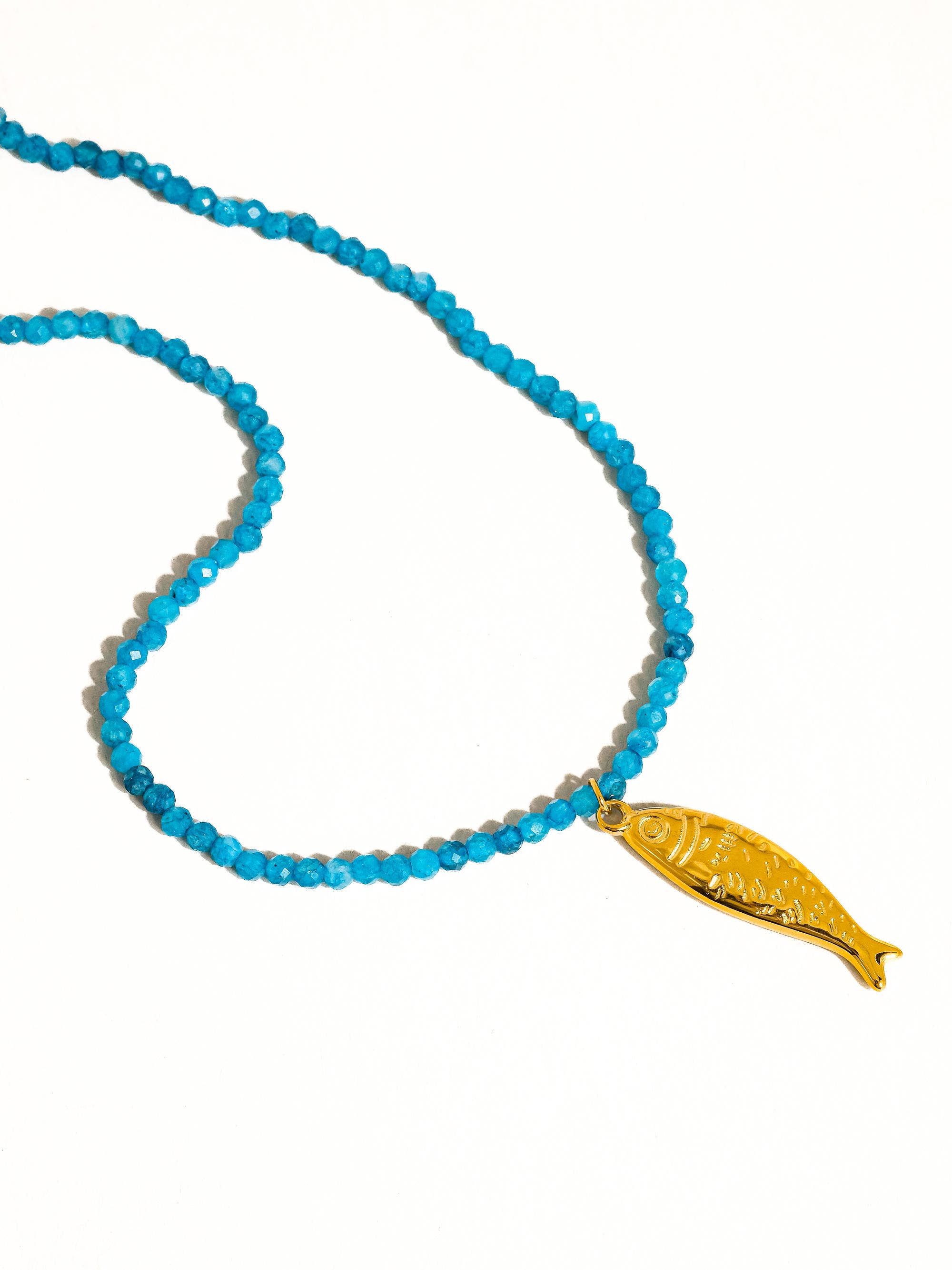 Blue beaded necklace with a gold fish-shaped pendant on a white background