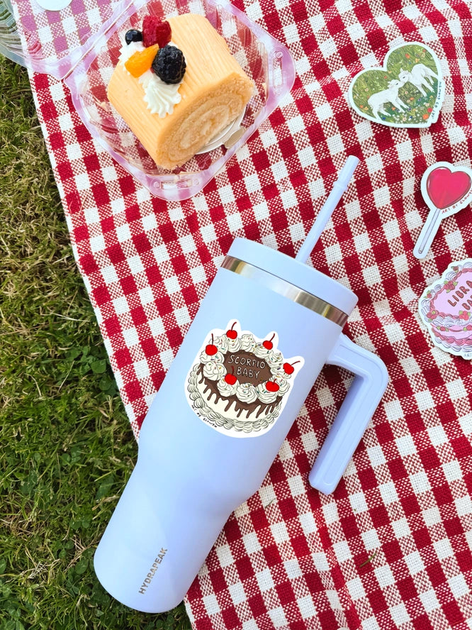 Light blue tumbler with cake design on a red and white checkered tablecloth with a dessert in the background.