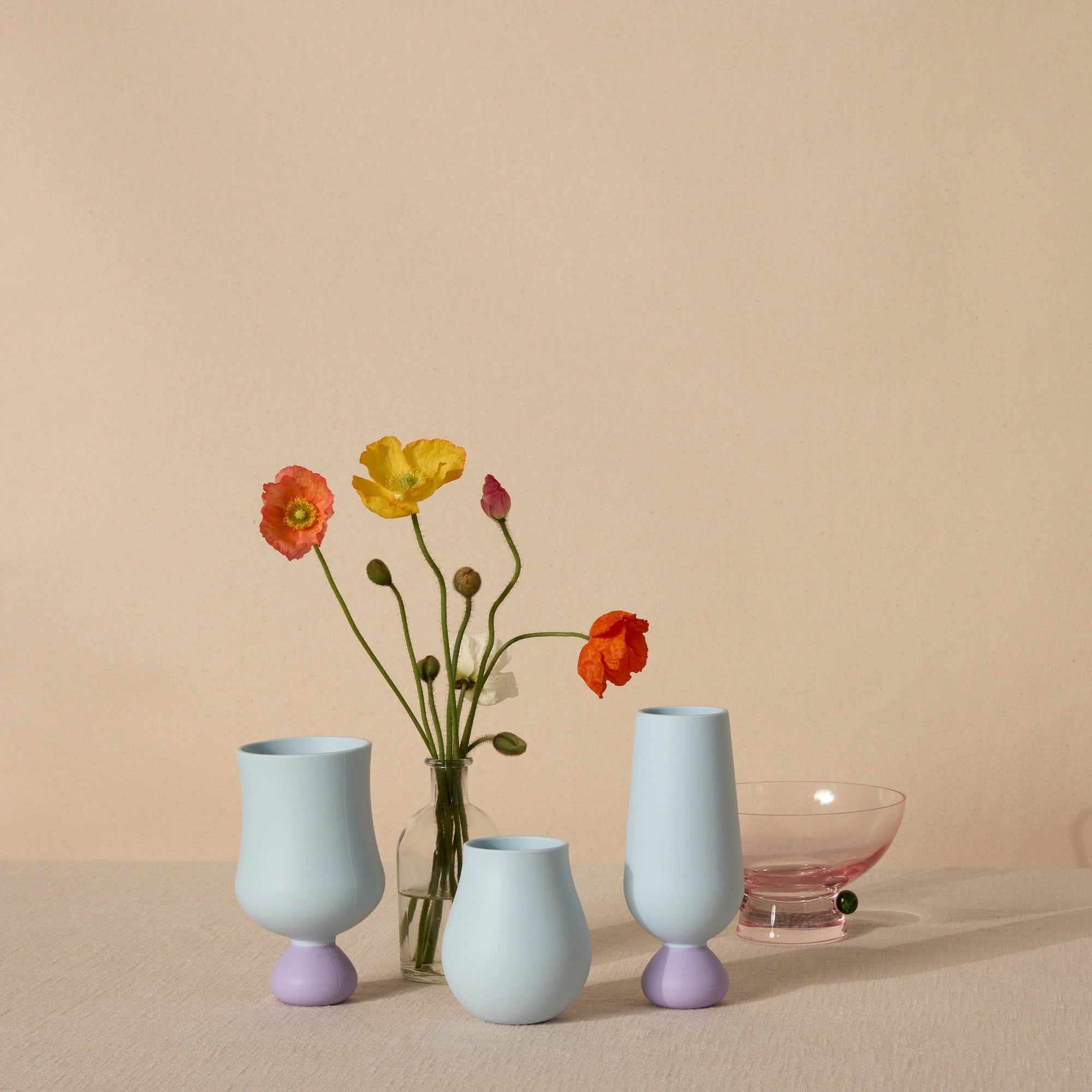 Three pastel-colored silicone cups with a clear vase containing flowers on a beige surface.