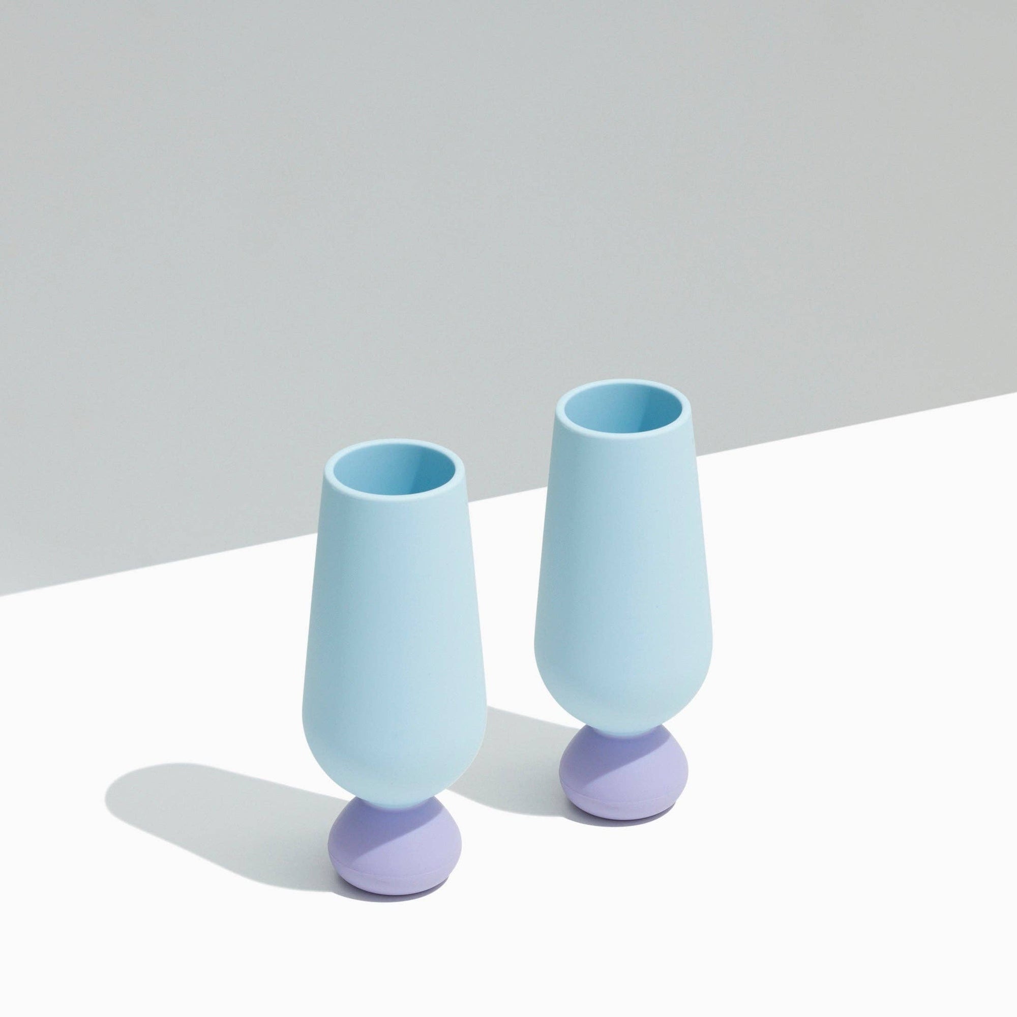 Two light blue silicone champagne flutes with purple bases on a white surface.