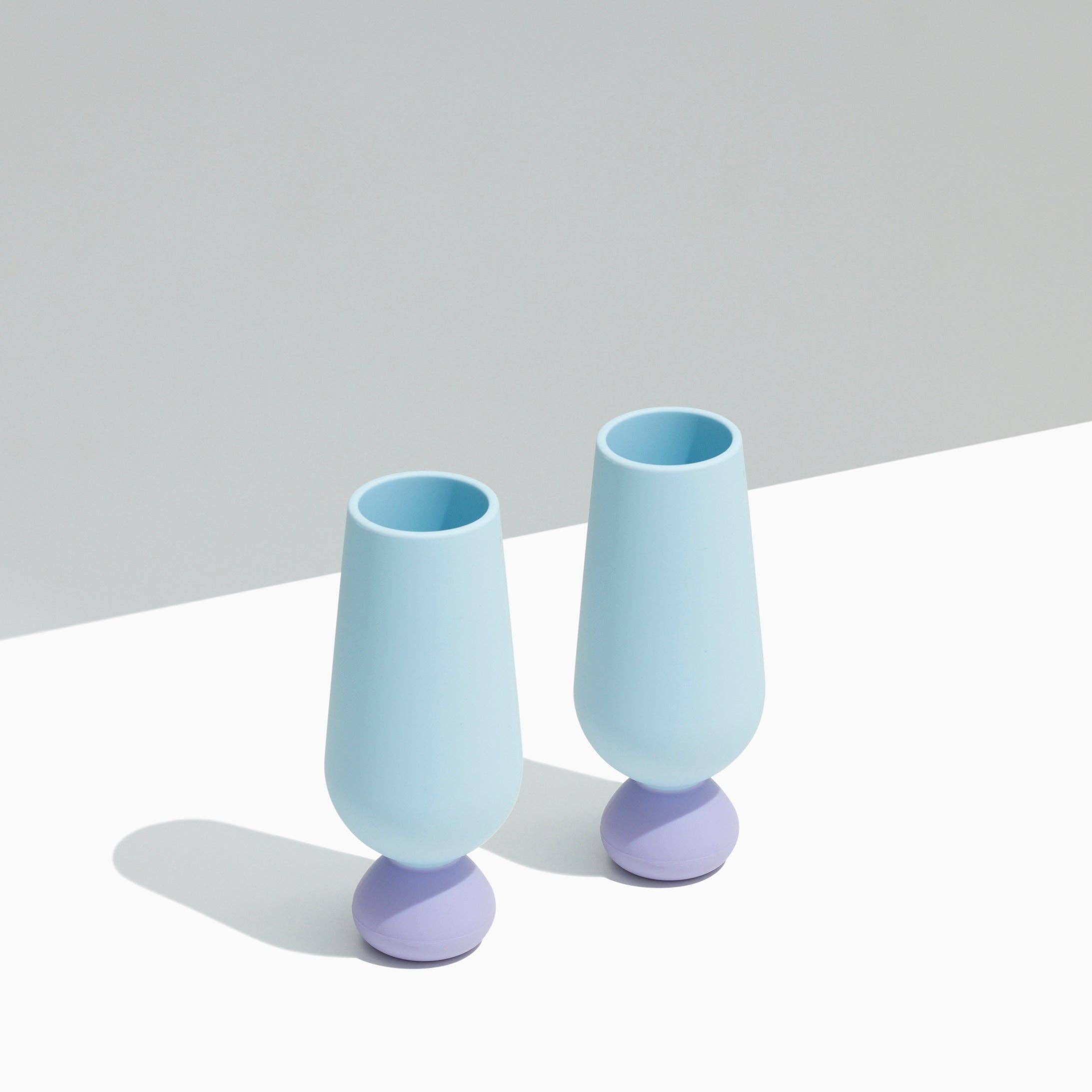 Two light blue silicone champagne flutes with purple bases on a white surface.