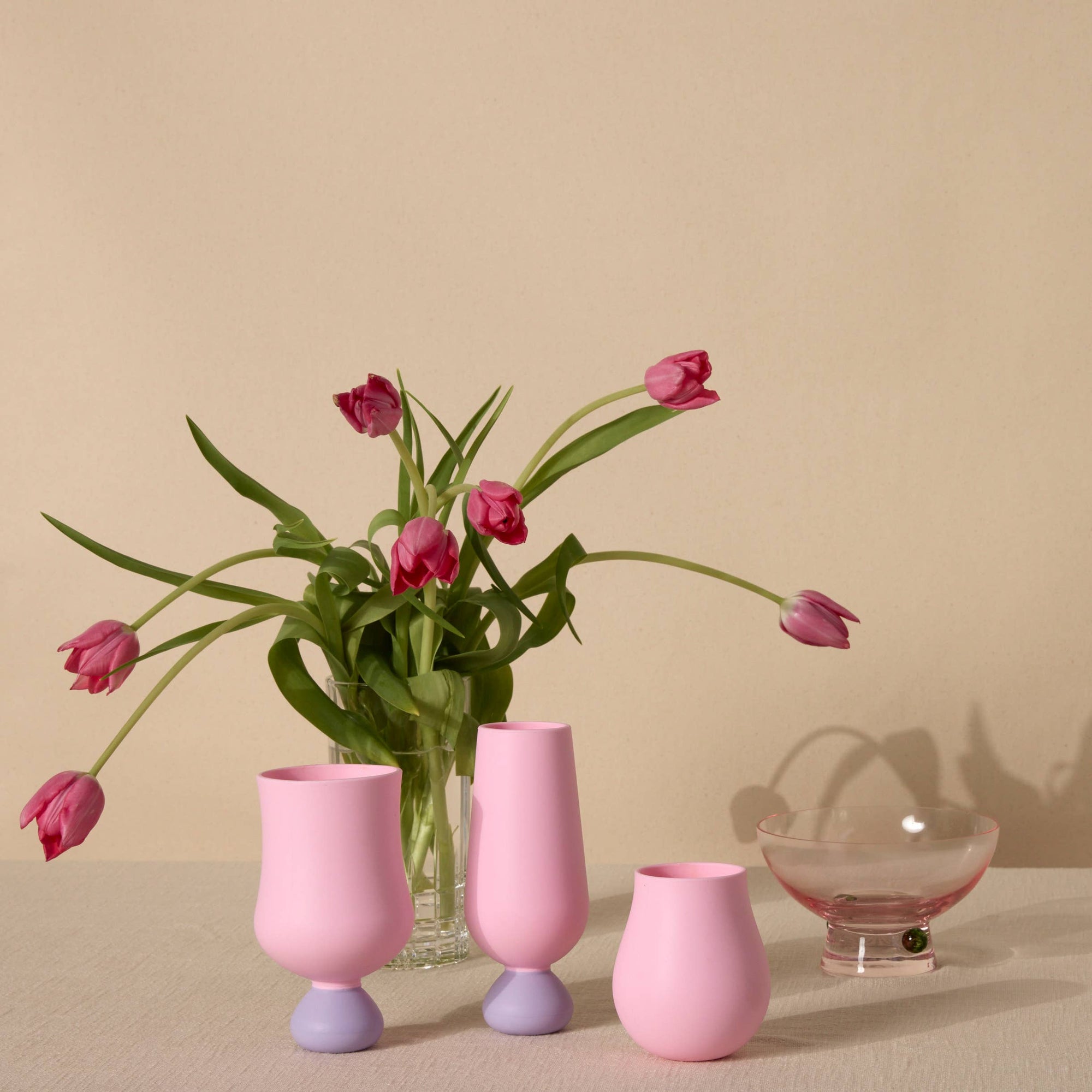 Three pink silicone cups with a glass bowl and pink tulips on a beige background