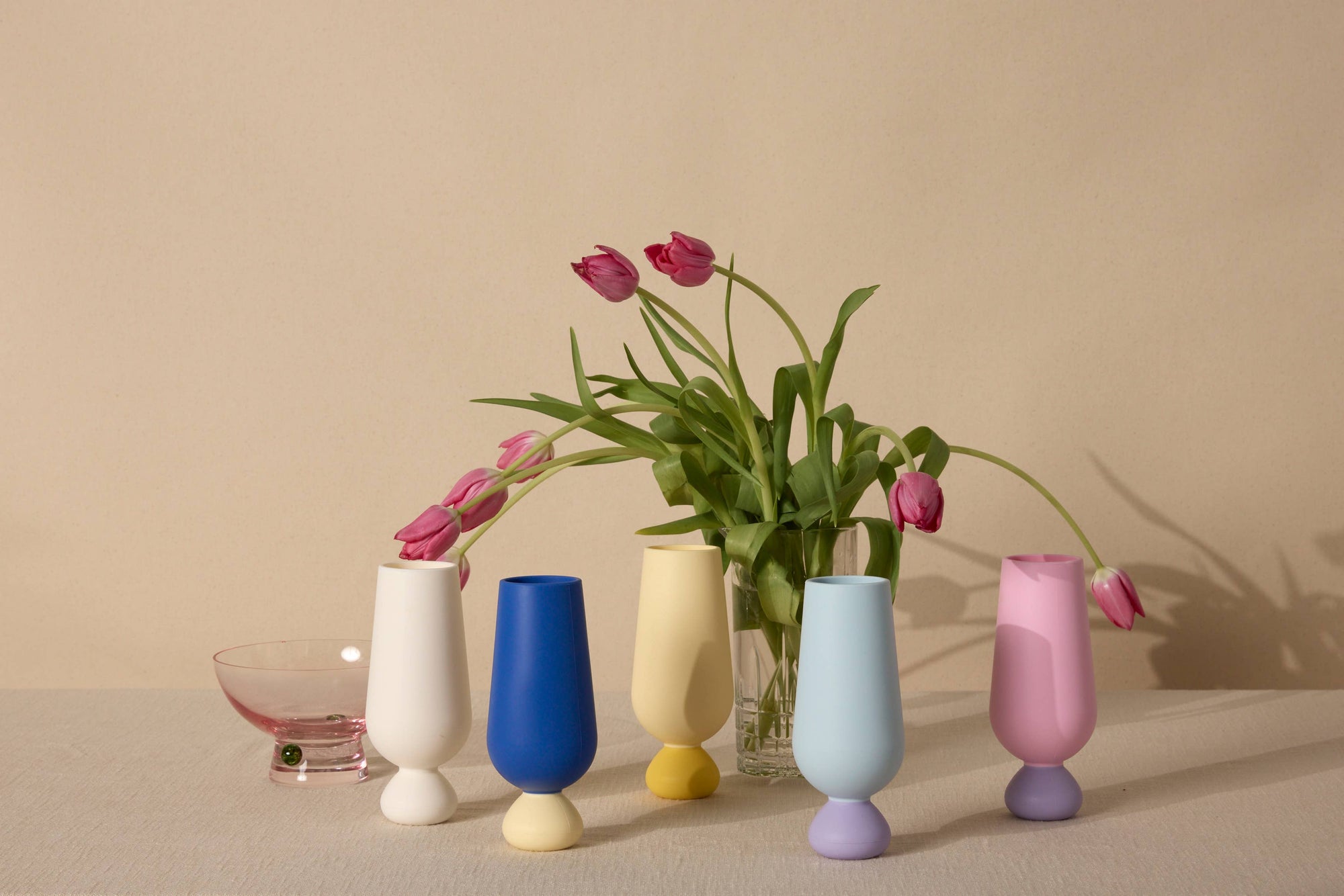 Set of colorful silicone unbreakable cups with a vase containing pink tulips on a beige background