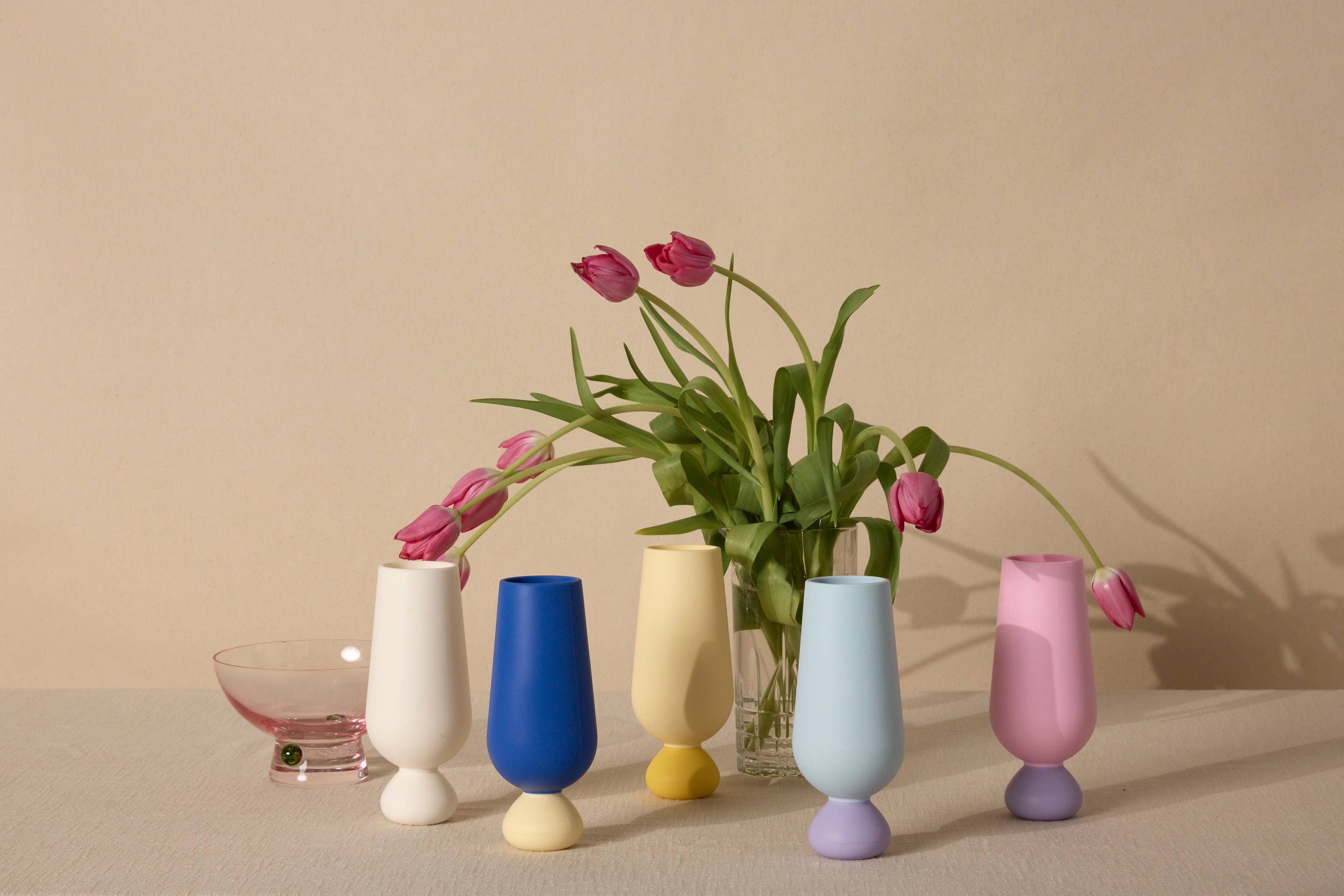 Set of colorful silicone unbreakable cups with a vase containing pink tulips on a beige background