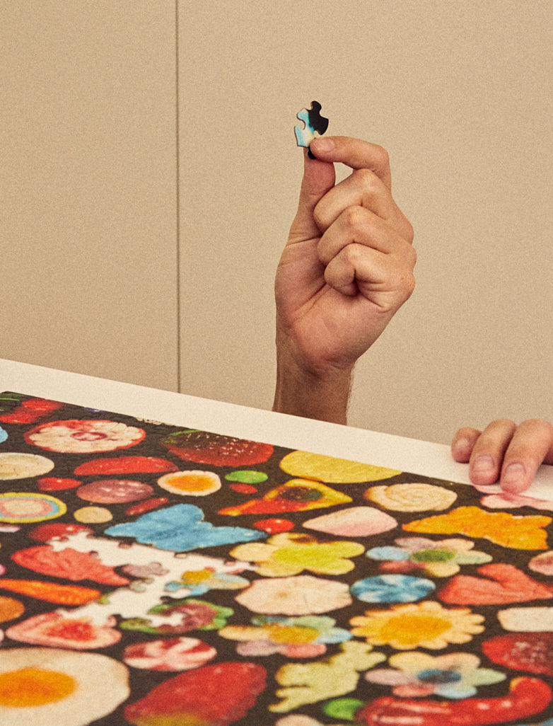 Hand holding a puzzle piece above a partially completed puzzle with colorful designs.