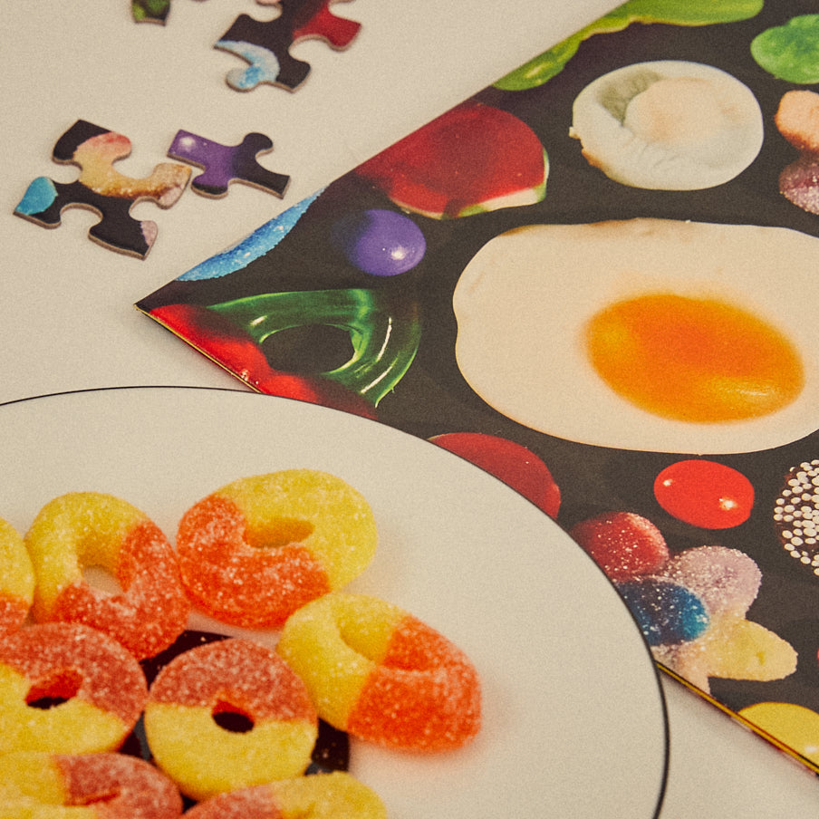 Colorful gummy candies on a plate with a partially completed puzzle featuring food images.