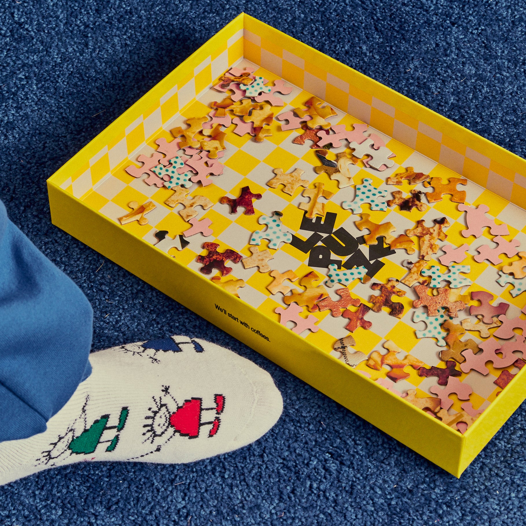 Colorful puzzle in a yellow box on a blue surface with a white sock featuring a design.