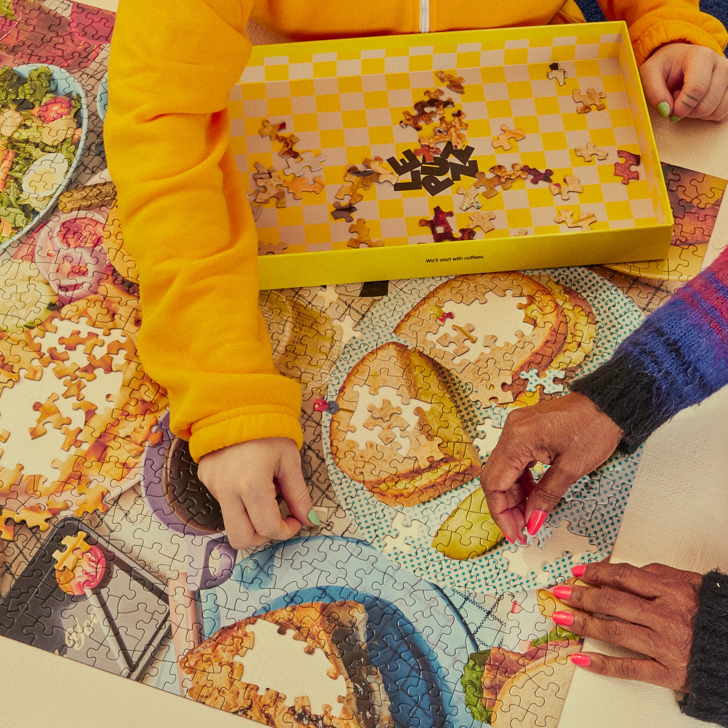 Two people working on a puzzle together, with one person wearing a yellow jacket and the other wearing a colorful sweater.