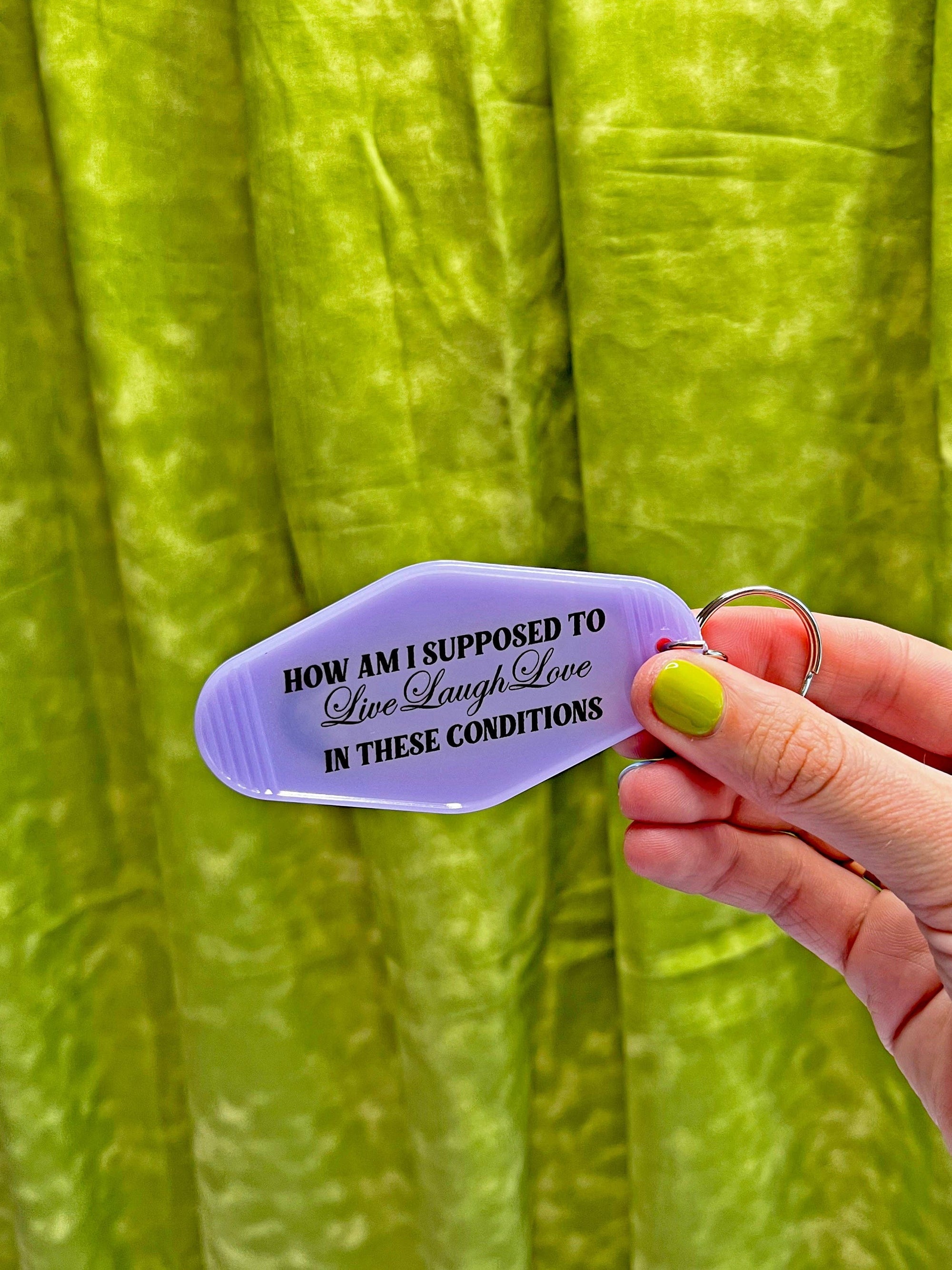 Hand holding a purple keychain with text against a green fabric background