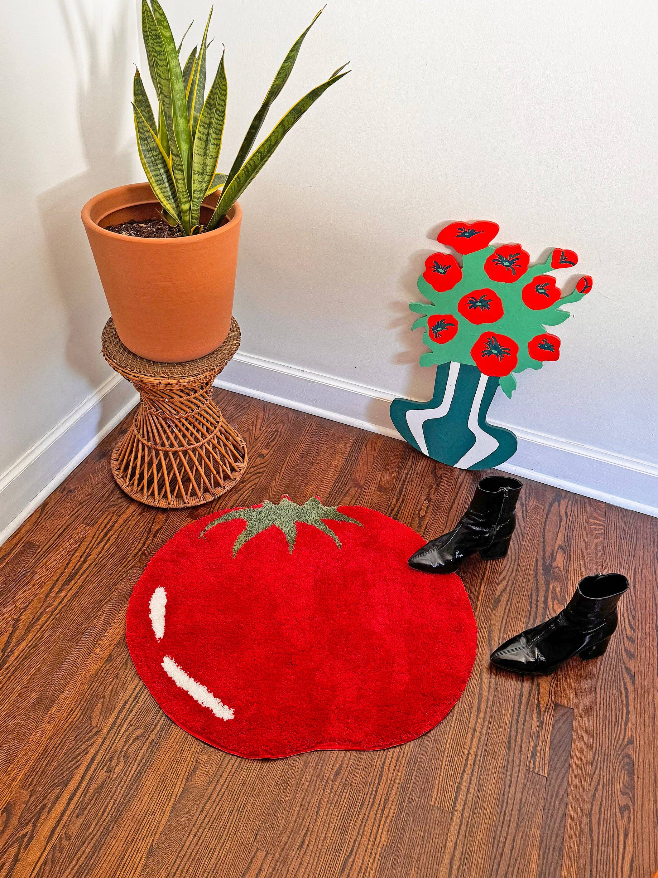 Red tomato-shaped rug on a wooden floor with a plant and shoes in the background.
