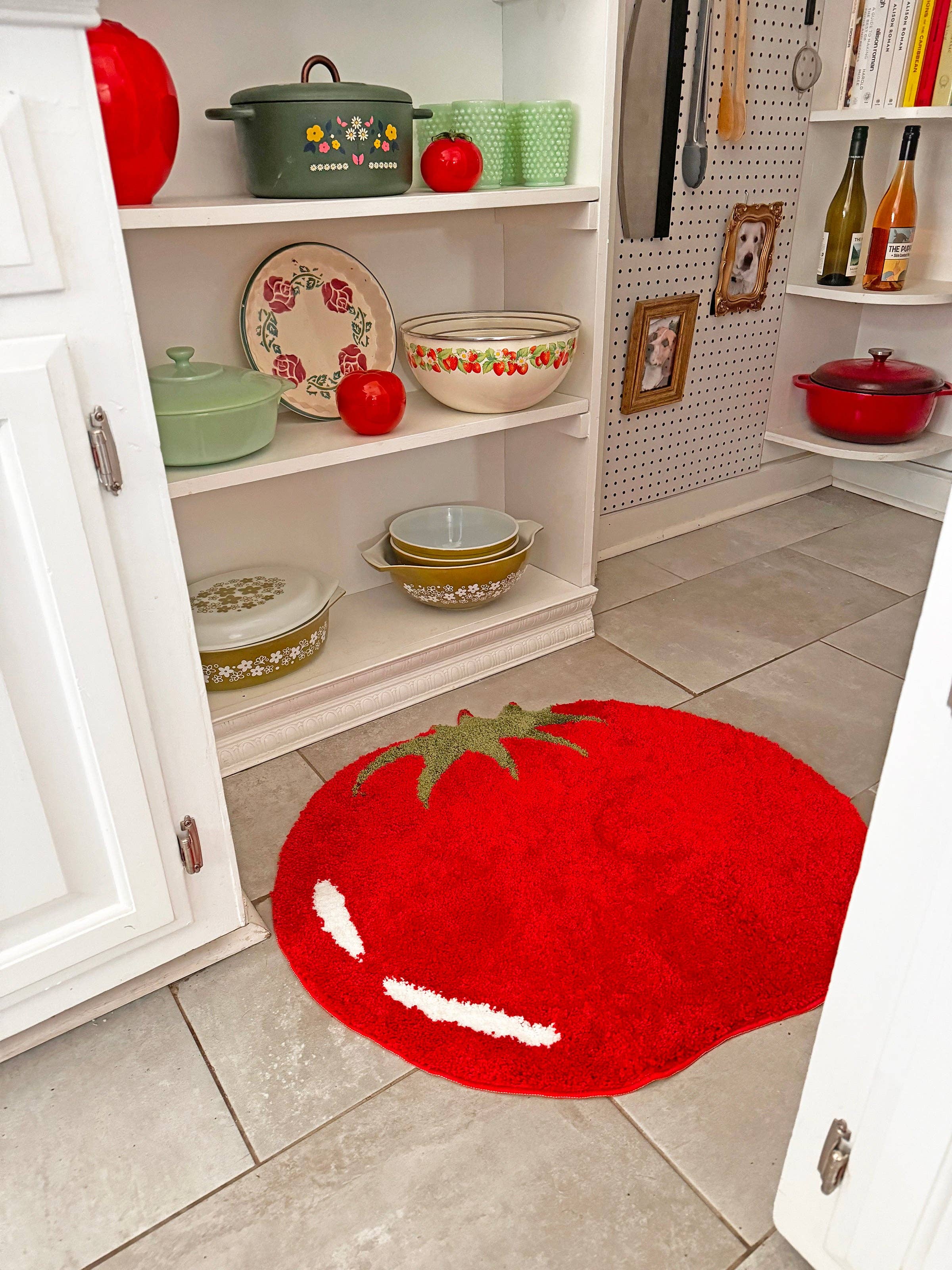 Kitchen with a tomato-shaped rug on the floor, shelves with kitchenware, and a pegboard wall.