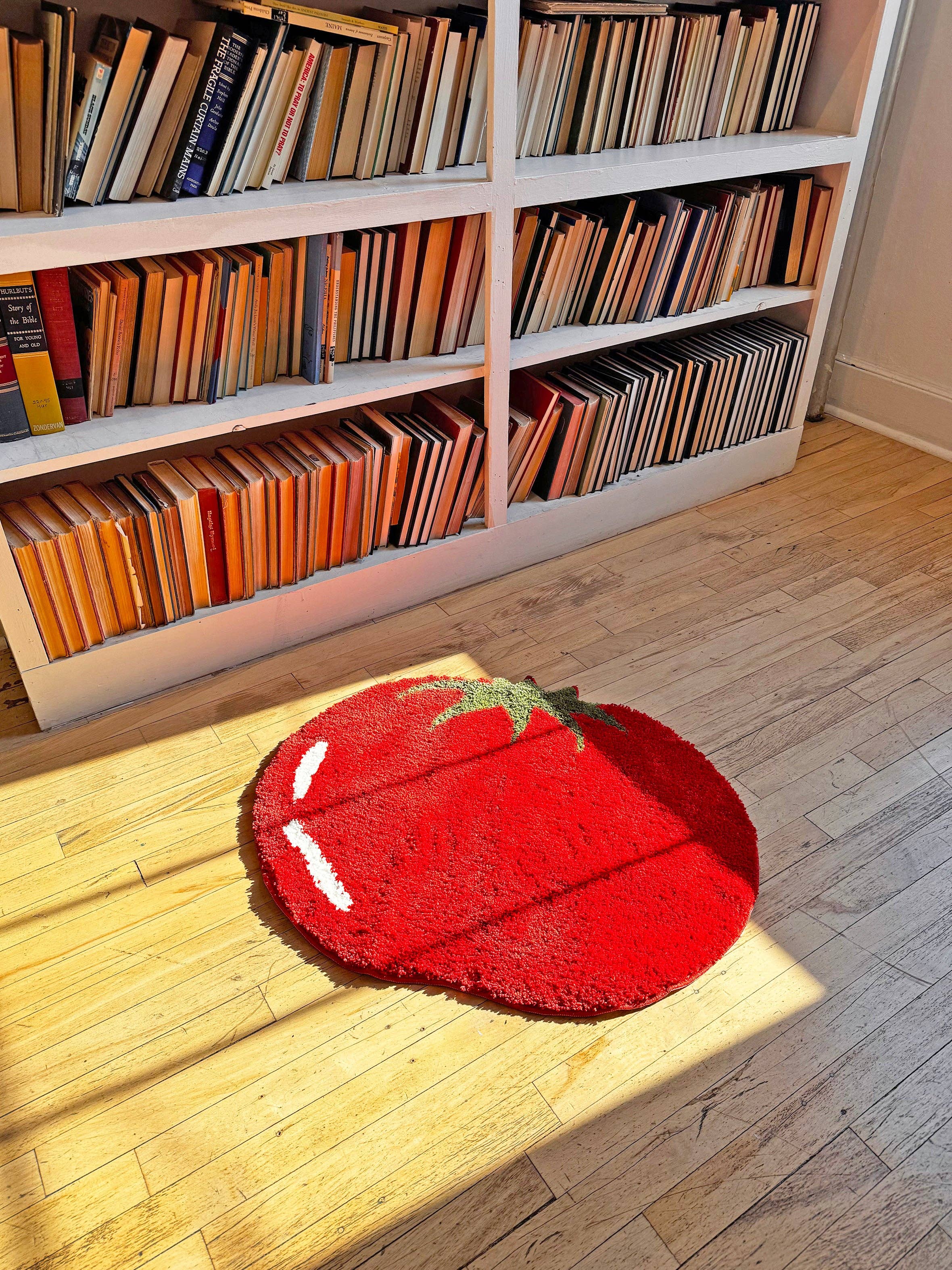 Red tomato-shaped rug on a wooden floor with bookshelves in the background