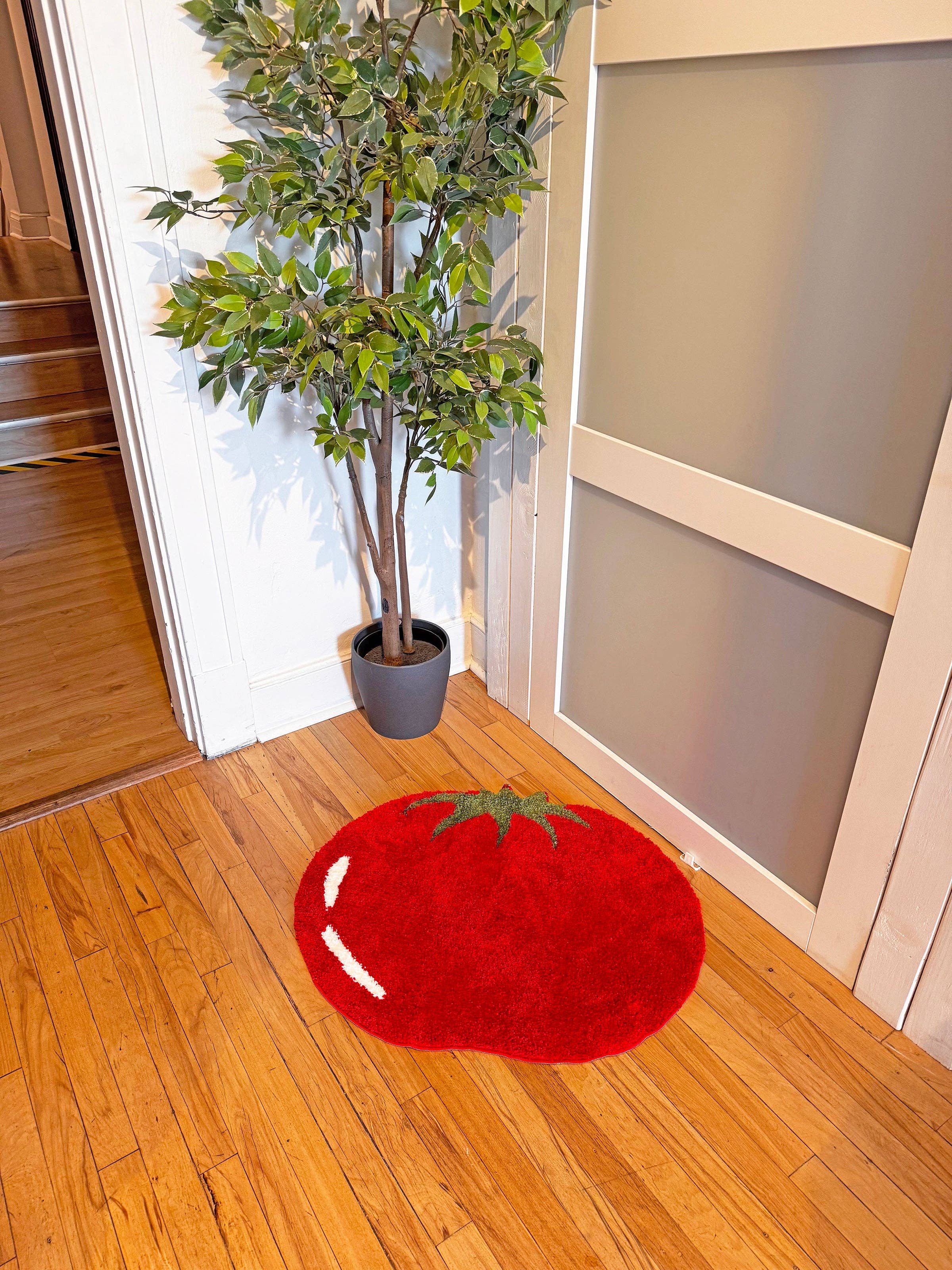 Red tomato-shaped rug on a wooden floor with a plant in the background