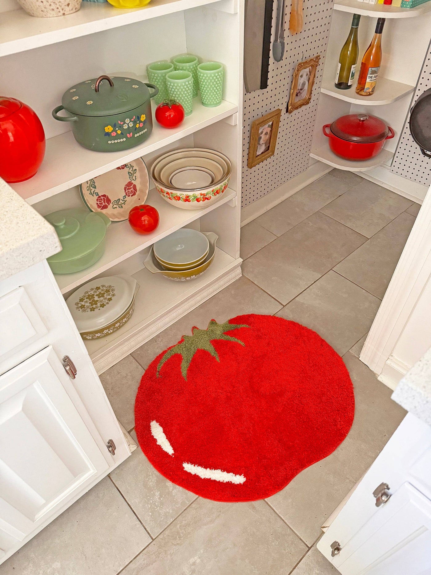 Red tomato-shaped rug on a kitchen floor with shelves containing kitchenware.
