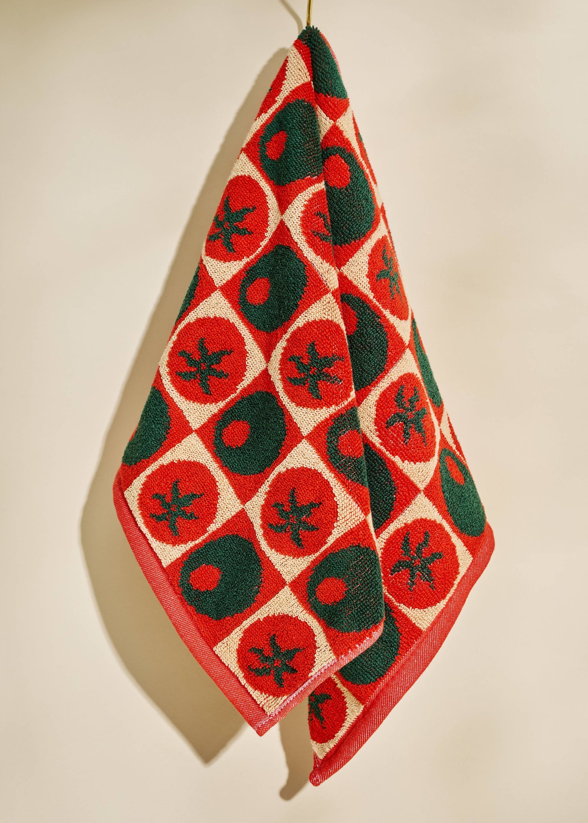 Decorative towel with red and green pattern hanging on a beige wall